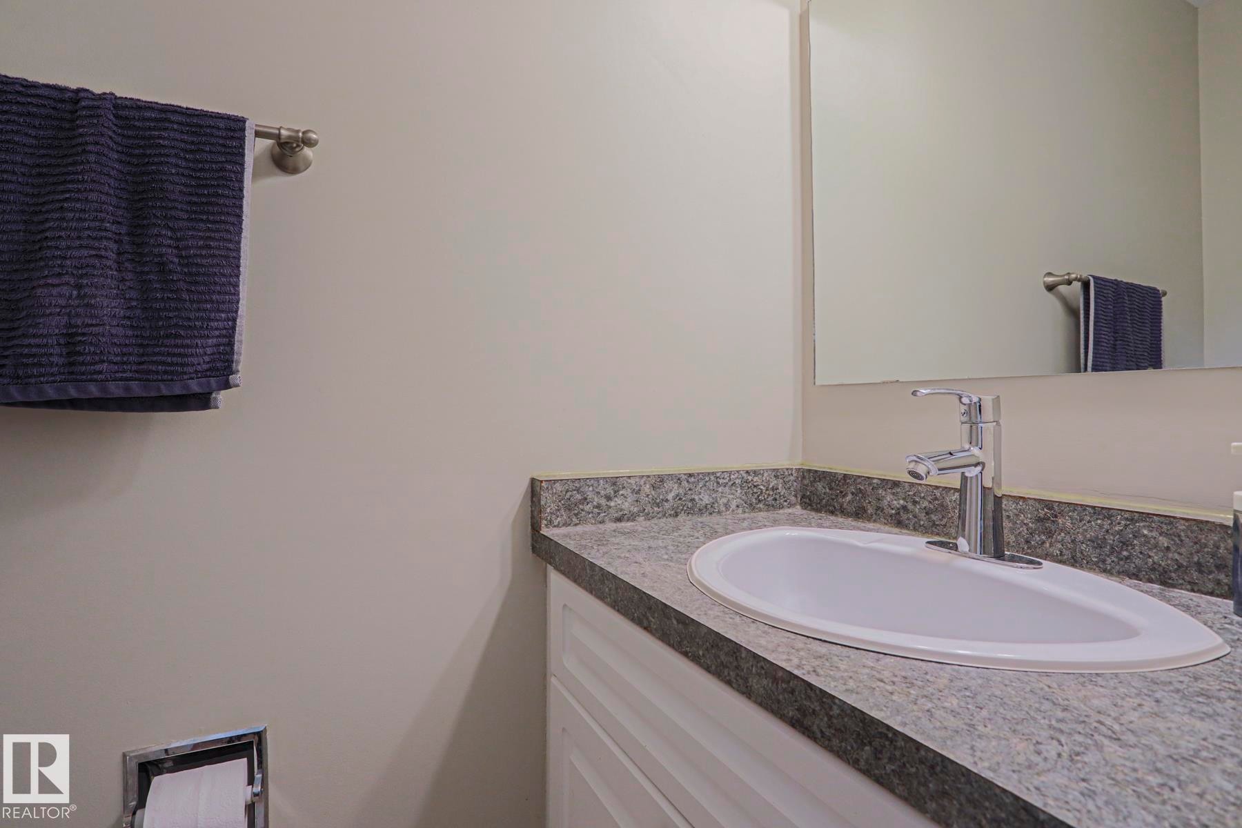 White vanity with a stone-finish countertop, integrated sink, and chrome faucet - 319 Telford Court, Leduc, AB