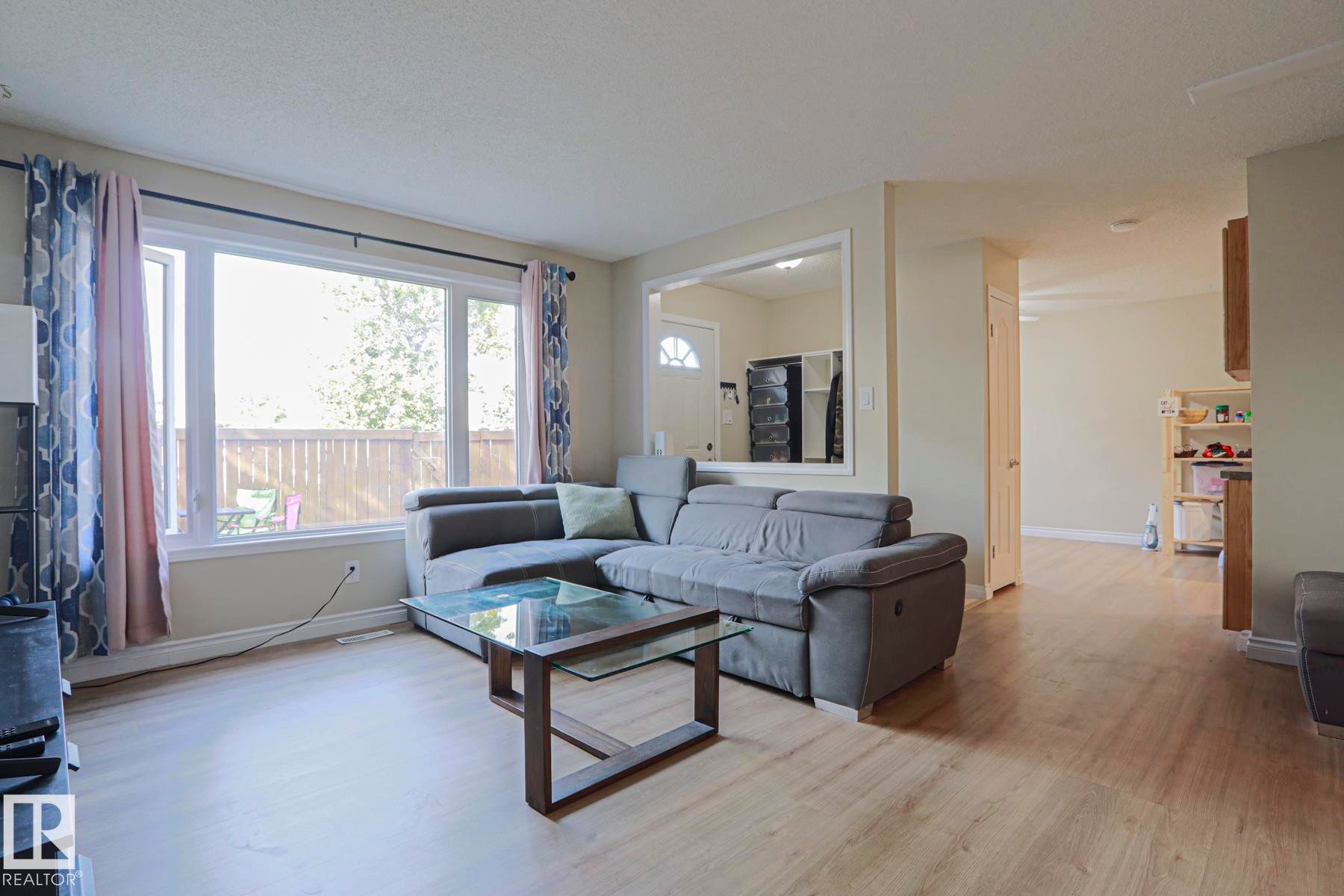 Expansive living area featuring light wood-finish flooring, a large window, and light-toned wall finishes - 319 Telford Court, Leduc, AB
