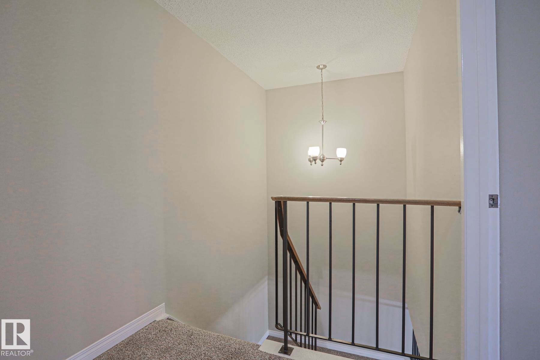 Staircase featuring carpeted steps, wrought iron railing with wood-finish top, and a ceiling-mounted chandelier - 319 Telford Court, Leduc, AB