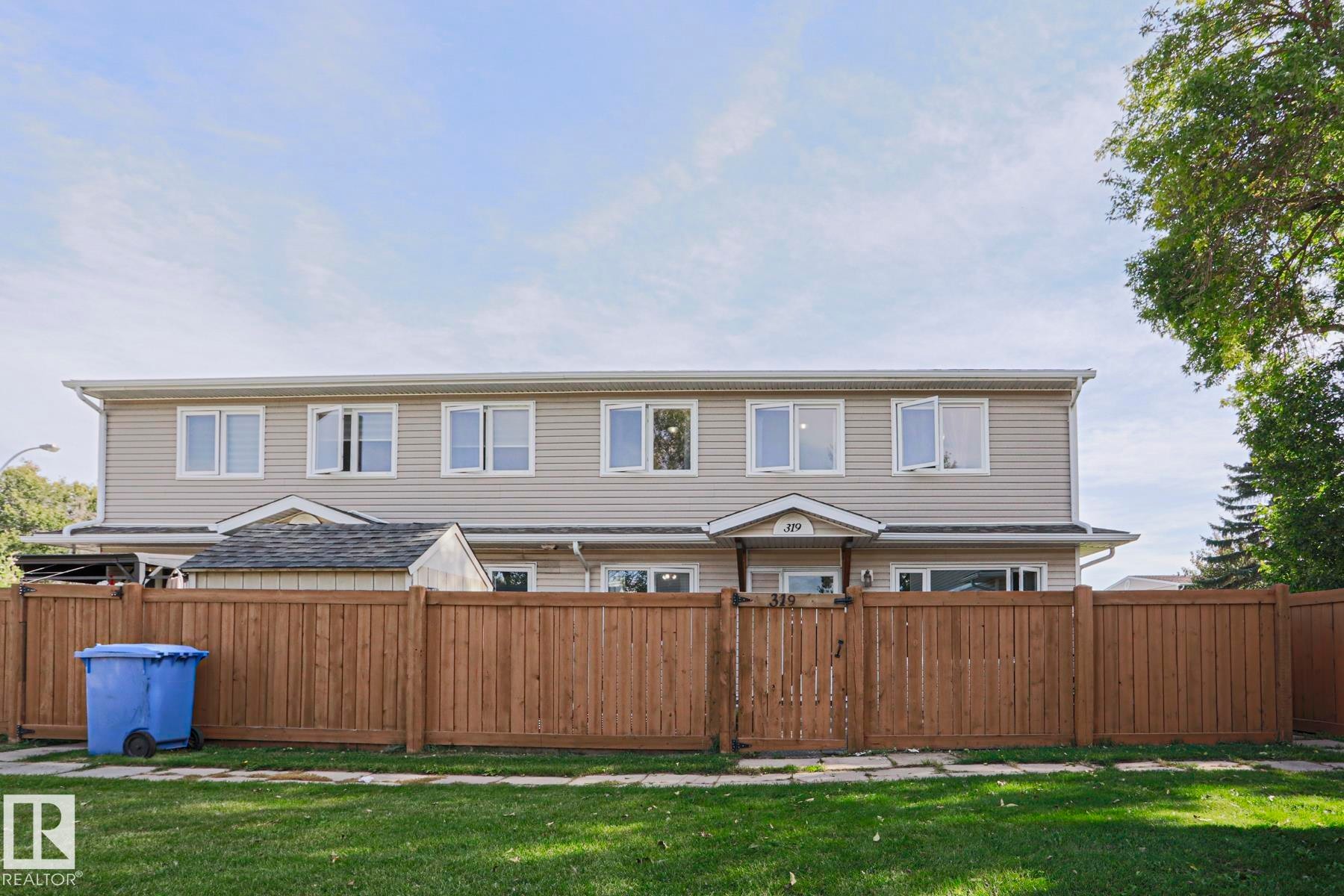 Siding exterior with multiple windows, featuring a brown privacy fence and a green lawn - 319 Telford Court, Leduc, AB