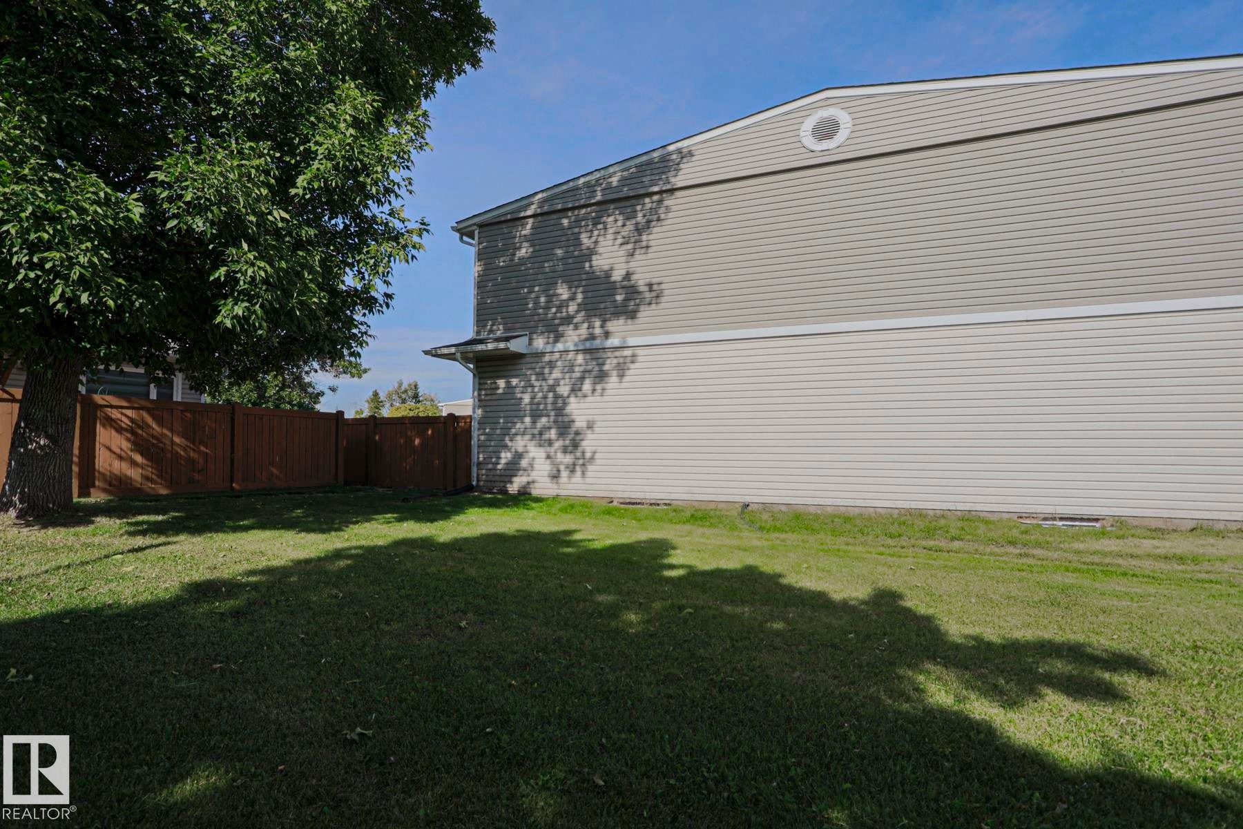 Manicured lawn with mature tree, brown privacy fencing, and grey horizontal siding - 319 Telford Court, Leduc, AB