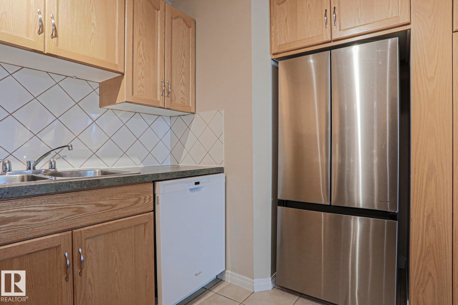 Stainless steel French door refrigerator, wood-finish cabinetry, tile backsplash, double basin sink, and white dishwasher - 319 Telford Court, Leduc, AB