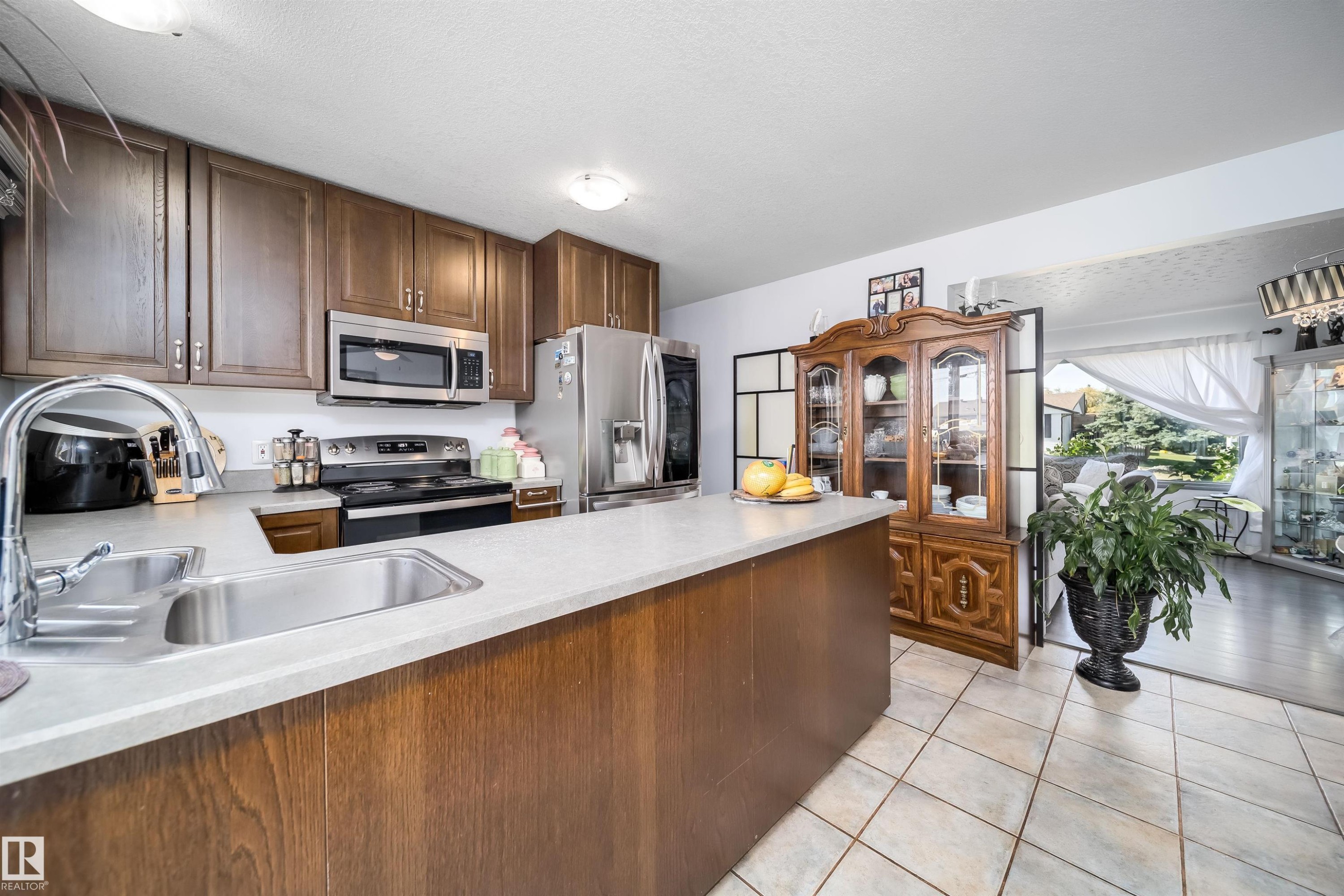 Kitchen featuring wood cabinetry, stainless steel appliances, light-toned countertops, and tile flooring - 10245 160 Street Nw, Edmonton, AB