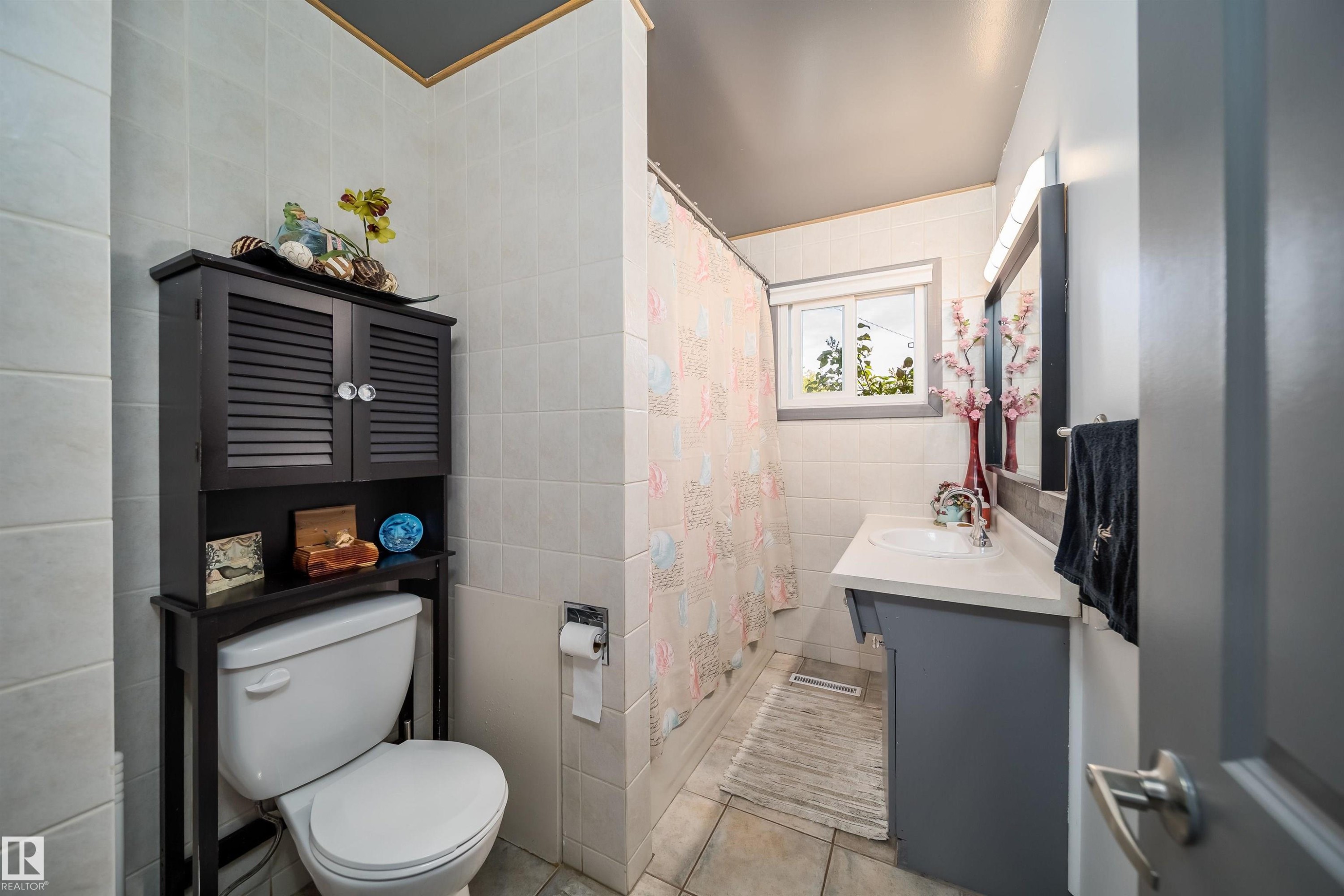 White tiled walls and flooring, complemented by a vanity with an integrated sink and a window providing natural light - 10245 160 Street Nw, Edmonton, AB