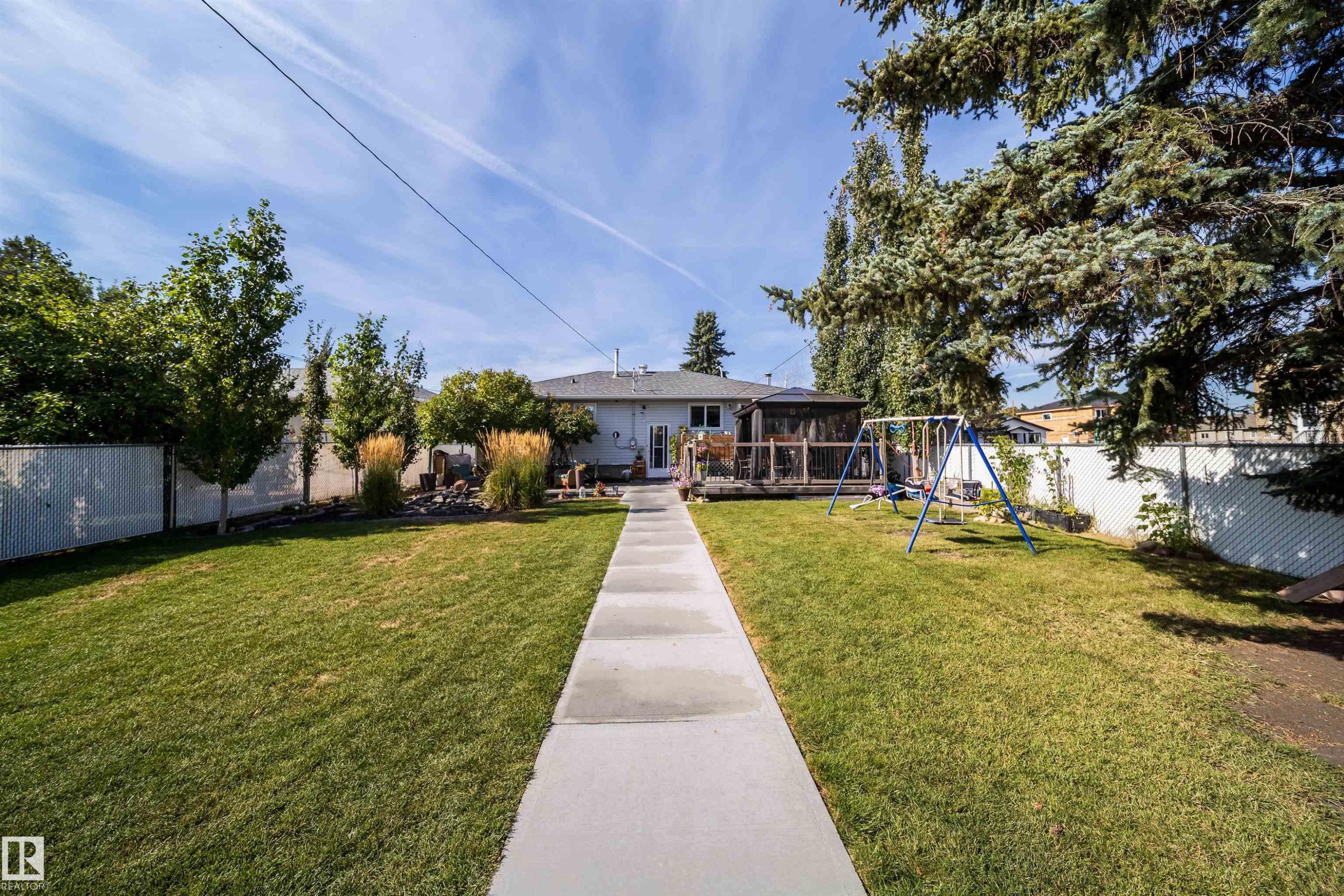 Expansive backyard featuring a central concrete pathway, a wooden deck with a screened enclosure, and mature trees - 10245 160 Street Nw, Edmonton, AB