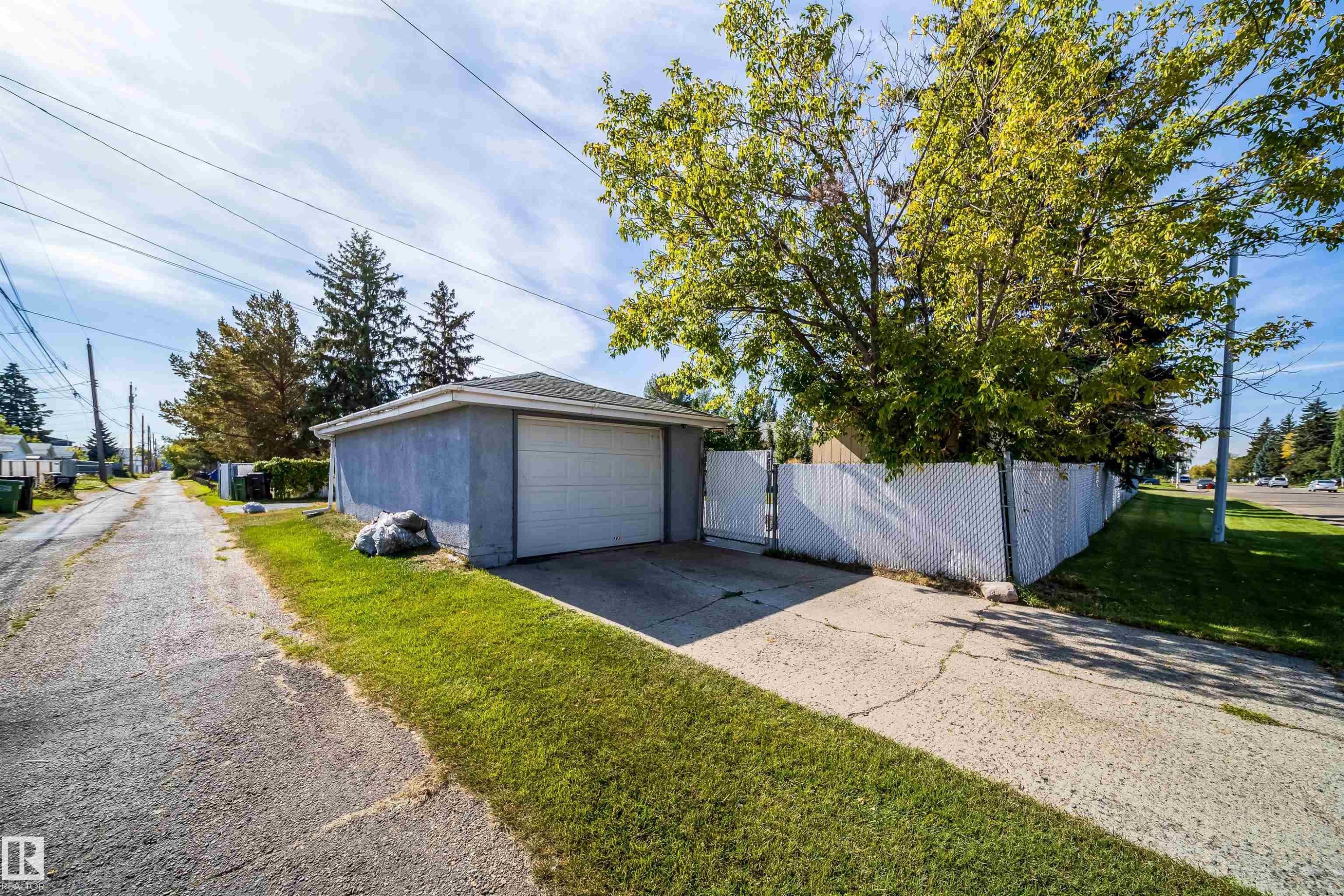 Detached garage featuring a white overhead door, concrete driveway, and white chain-link fencing - 10245 160 Street Nw, Edmonton, AB