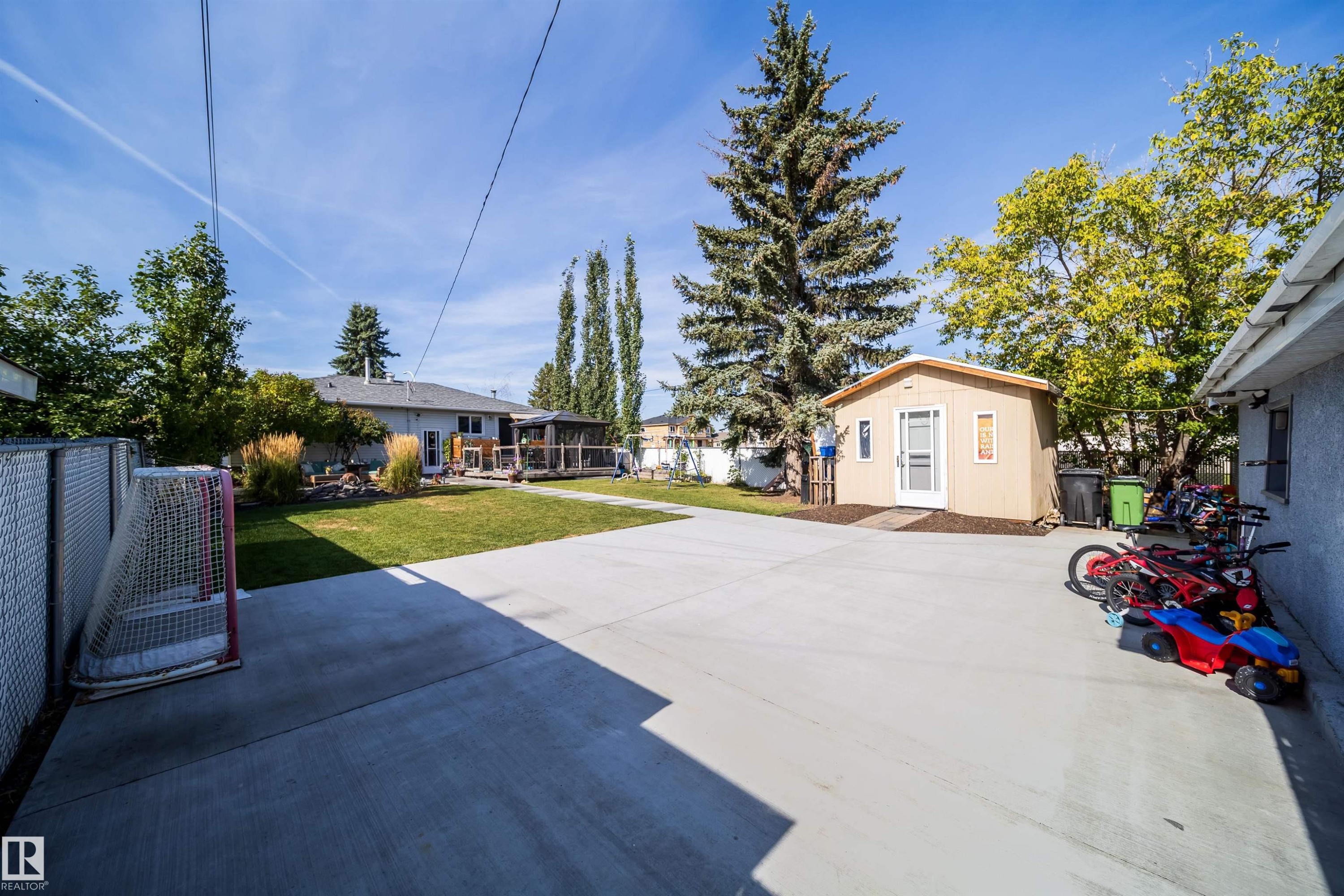 Expansive concrete patio with a detached shed, chain-link fence, and mature trees - 10245 160 Street Nw, Edmonton, AB