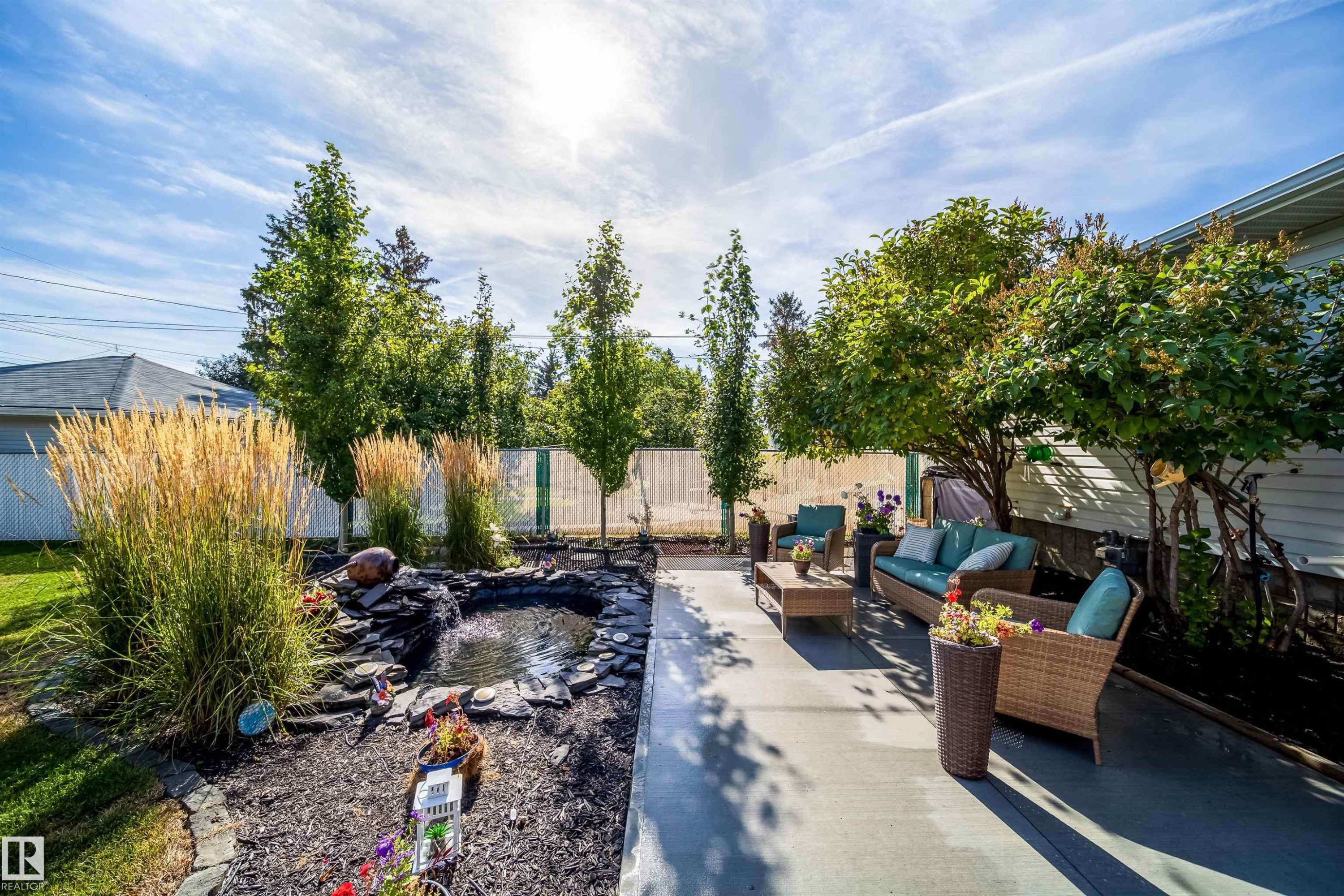 Concrete patio with mature trees, a rock-lined pond, and tall ornamental grasses - 10245 160 Street Nw, Edmonton, AB