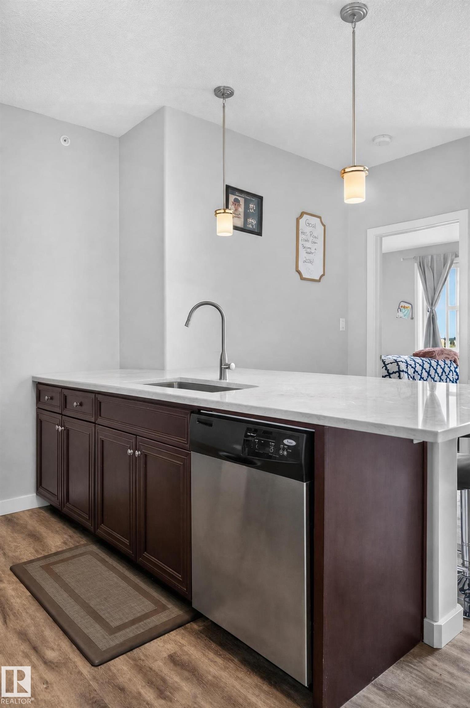 Kitchen island featuring dark wood cabinetry, a stainless steel dishwasher, a single-basin sink with a gooseneck faucet, and white countertops - #411 304 Ambleside Link Li Sw, Edmonton, AB