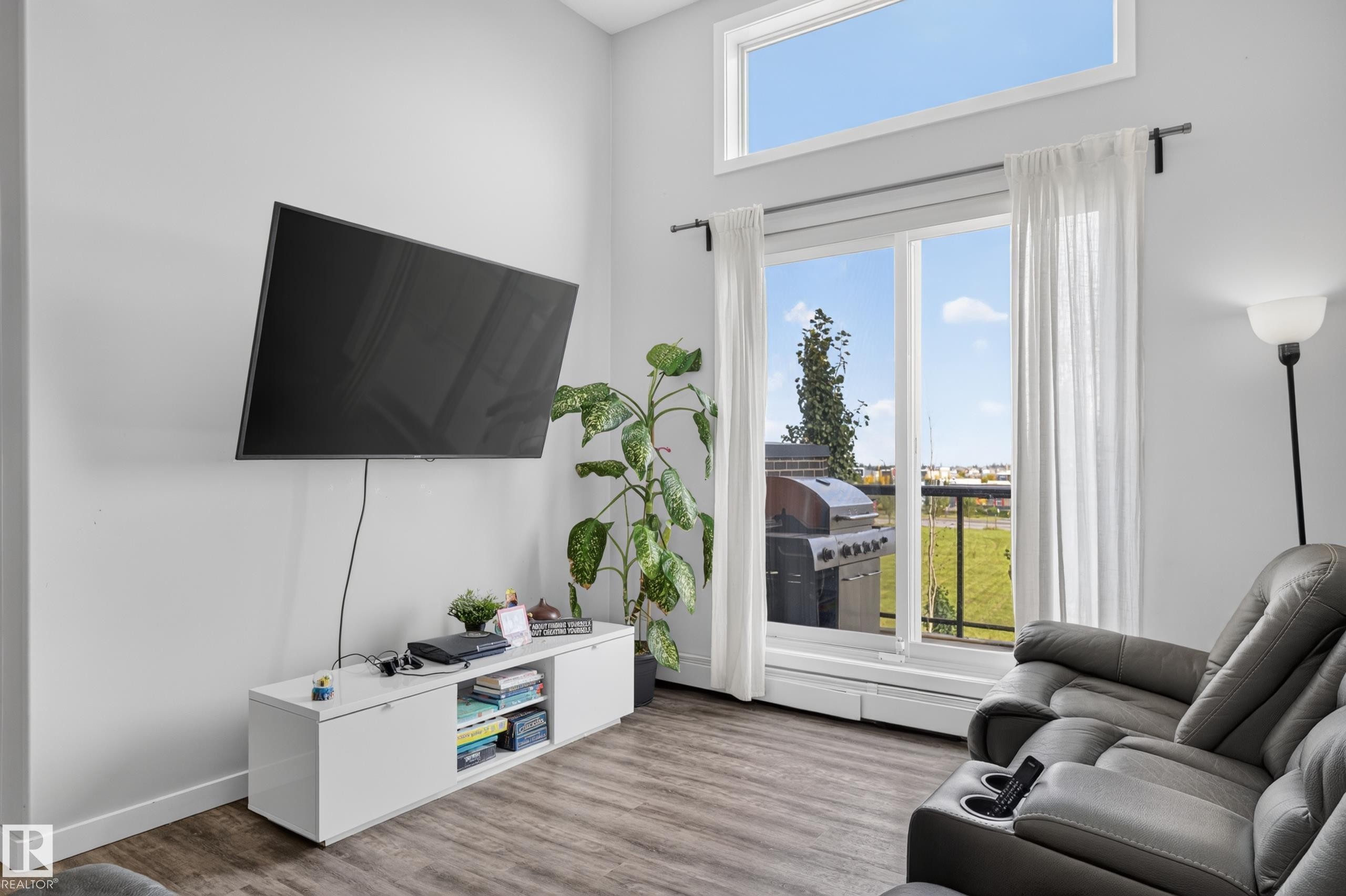 Wood-finish flooring, white walls, and a large window with an upper transom window - #411 304 Ambleside Link Li Sw, Edmonton, AB