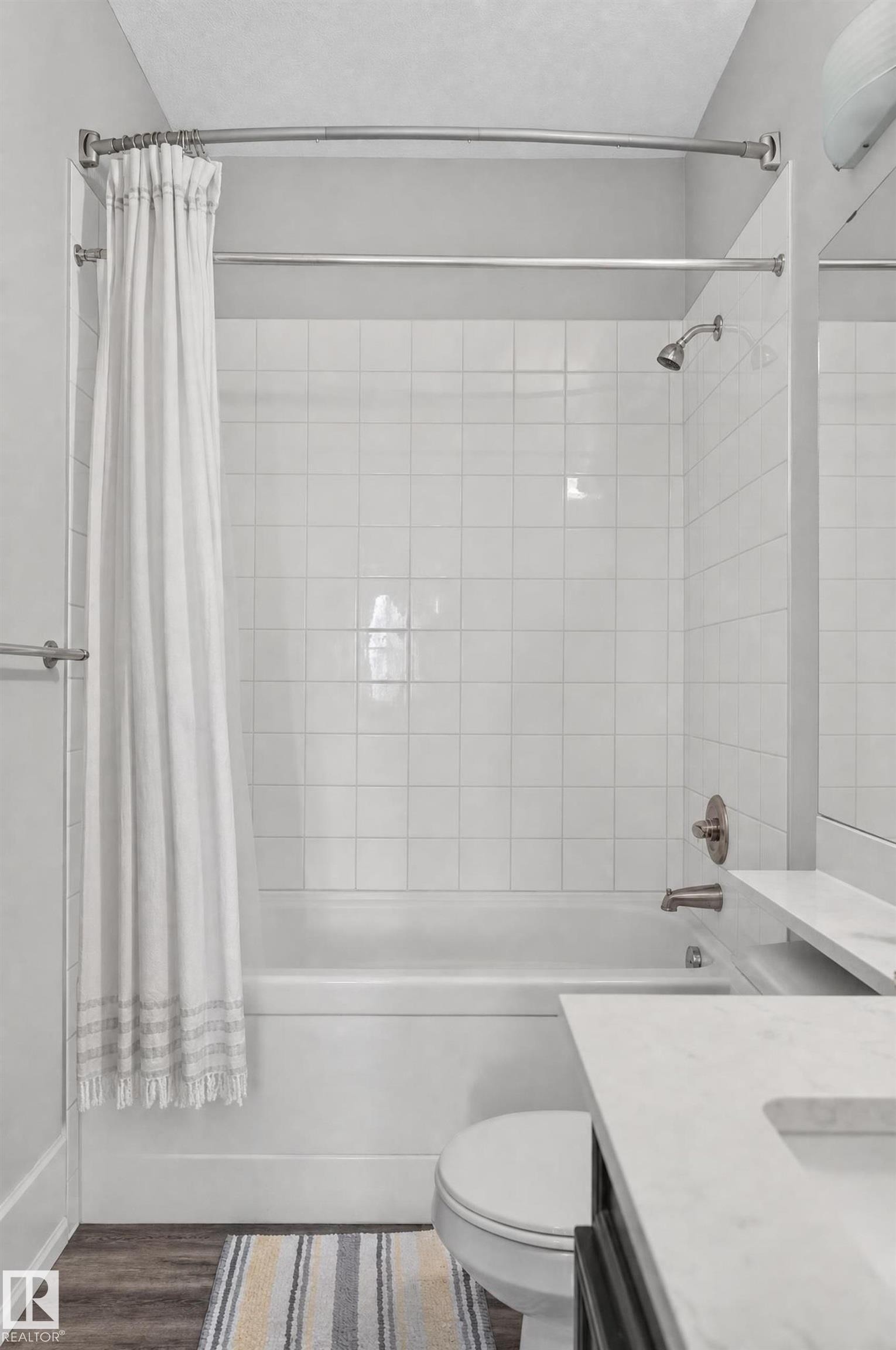 Bathtub with white square tile surround, brushed nickel fixtures, and wood-finish flooring - #411 304 Ambleside Link Li Sw, Edmonton, AB