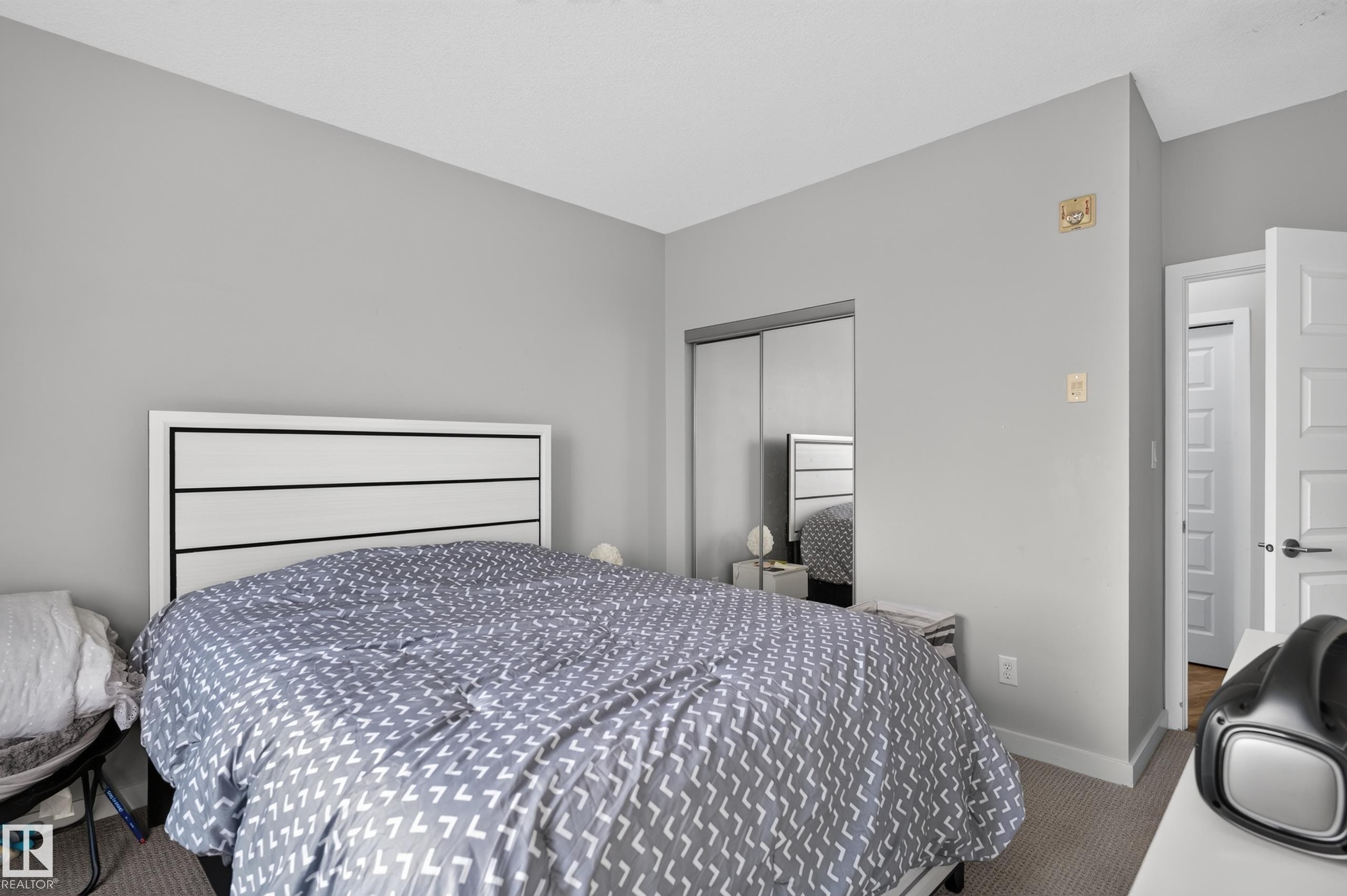 Carpeted flooring with light gray walls, white trim, and a mirrored closet door - #411 304 Ambleside Link Li Sw, Edmonton, AB