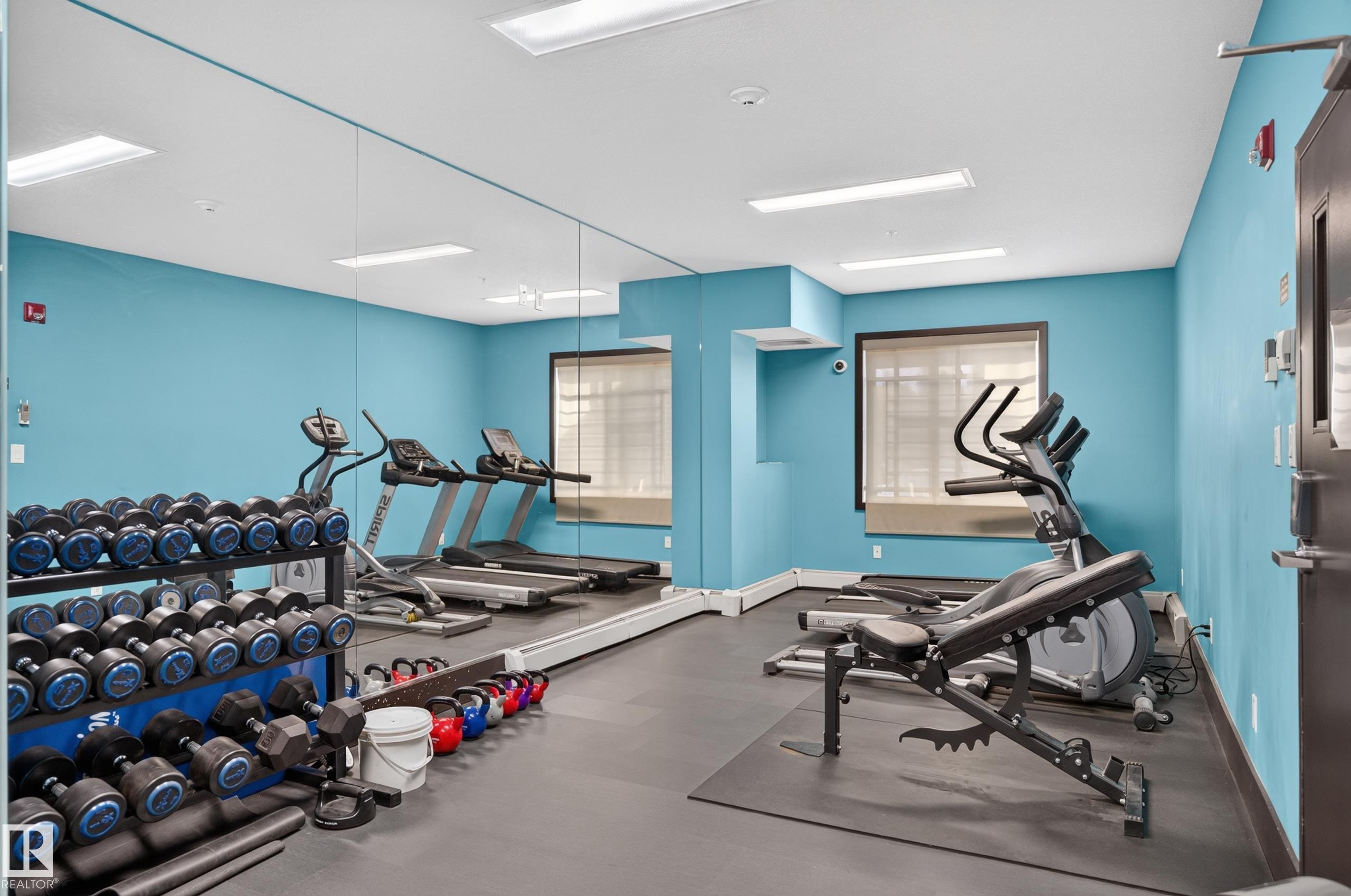 Fitness center featuring a mirrored wall, integrated lighting, and durable rubber flooring - #411 304 Ambleside Link Li Sw, Edmonton, AB