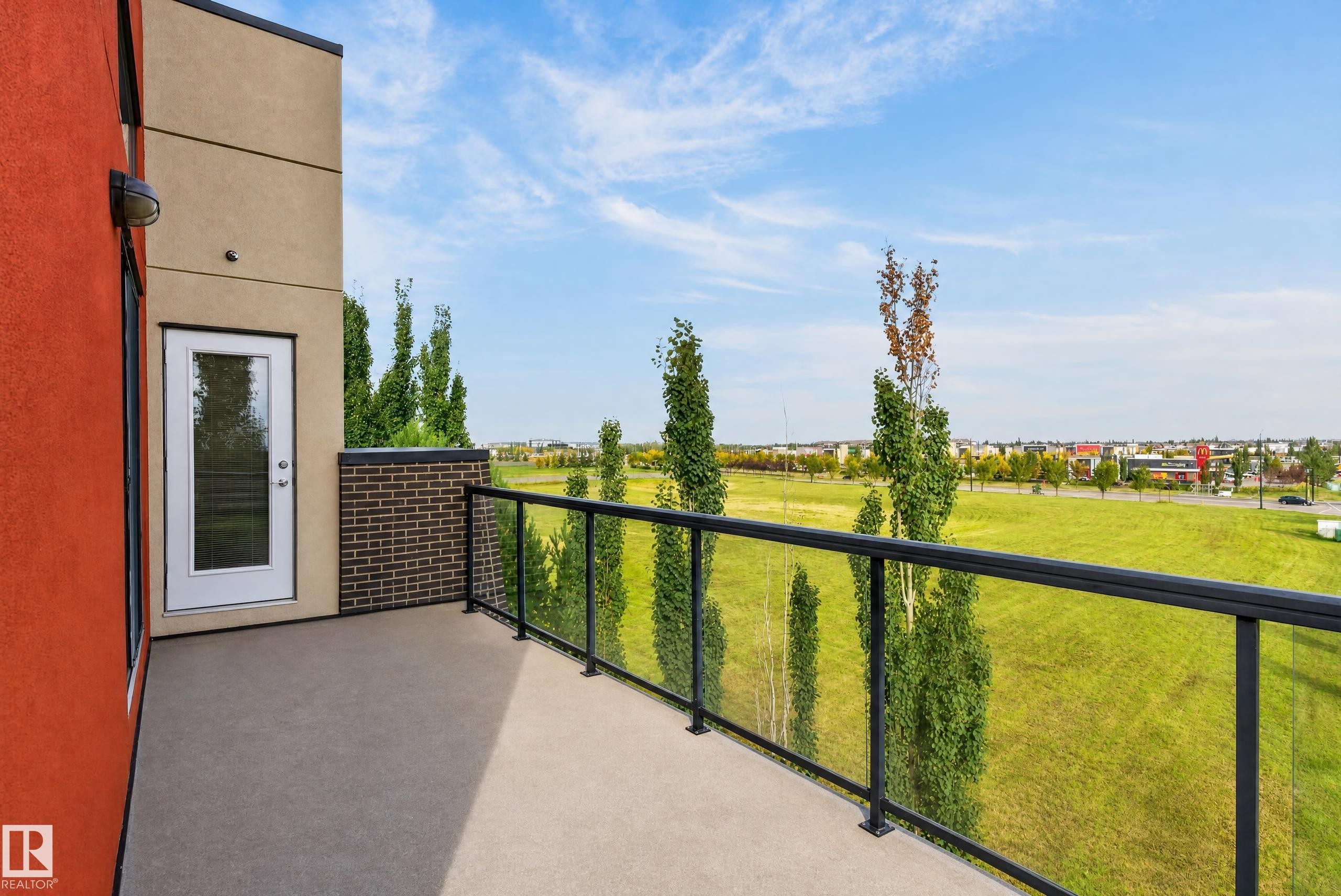 Private outdoor balcony with a glass railing system and a solid brick accent wall - #411 304 Ambleside Link Li Sw, Edmonton, AB