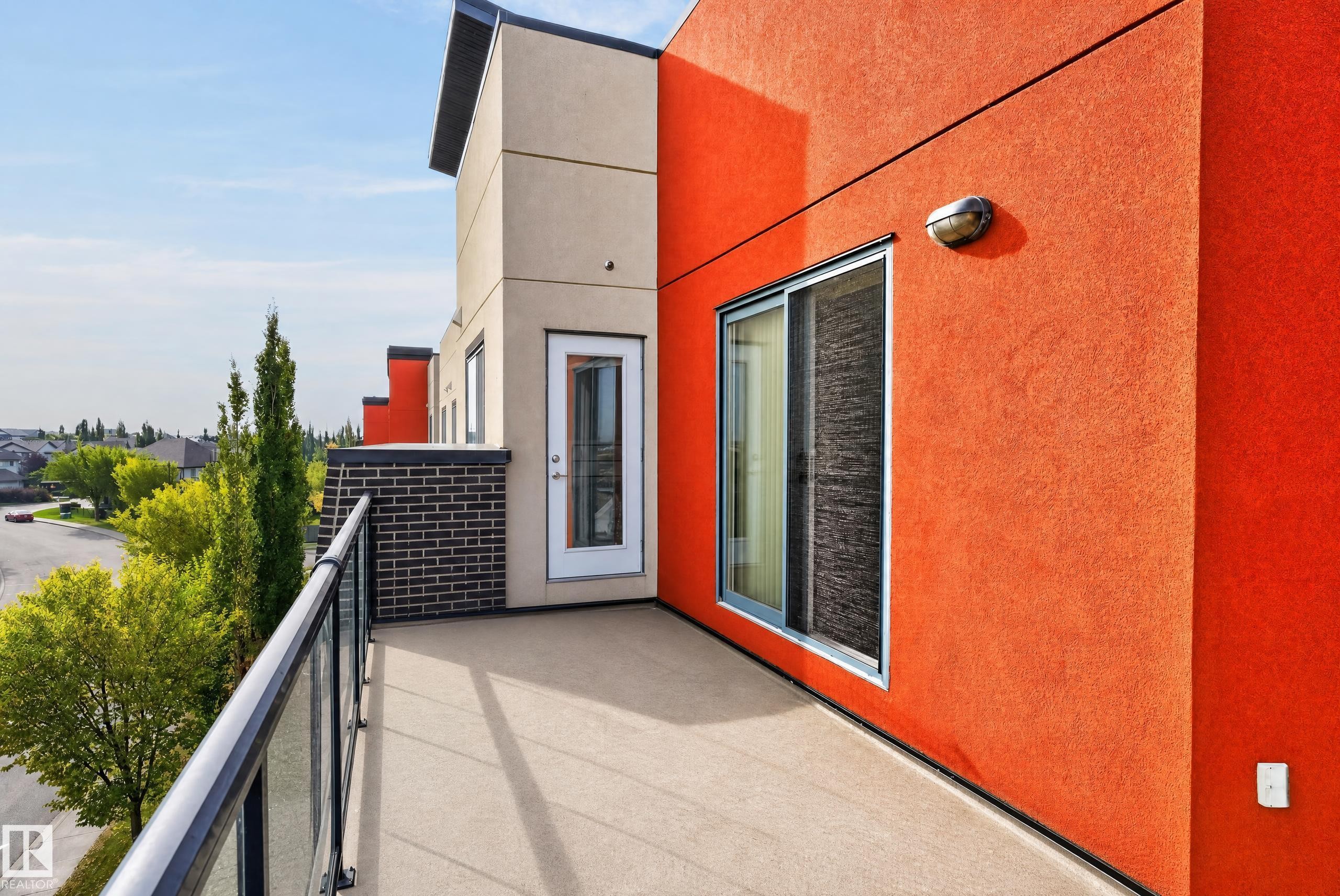 Private balcony featuring a glass and metal railing, textured stucco exterior, and sliding glass door access - #411 304 Ambleside Link Li Sw, Edmonton, AB