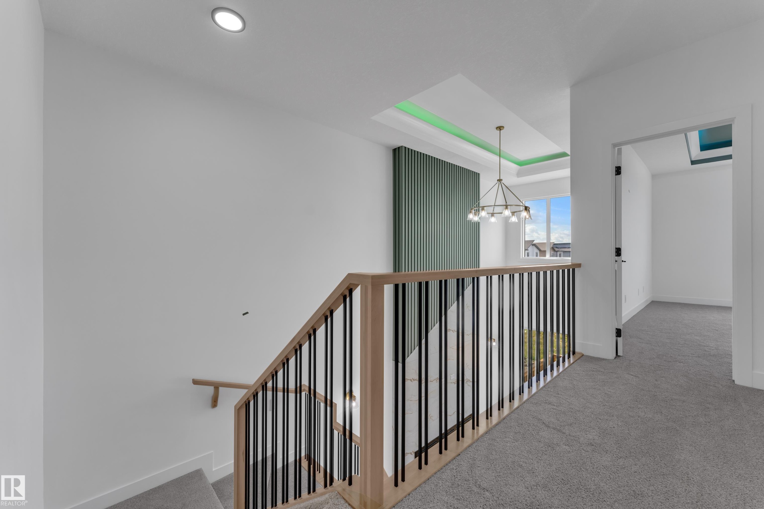 Open landing with light-colored carpeting, a contemporary chandelier, a coffered ceiling with accent lighting, and a slatted accent wall - 4212 63 Street, Beaumont, AB