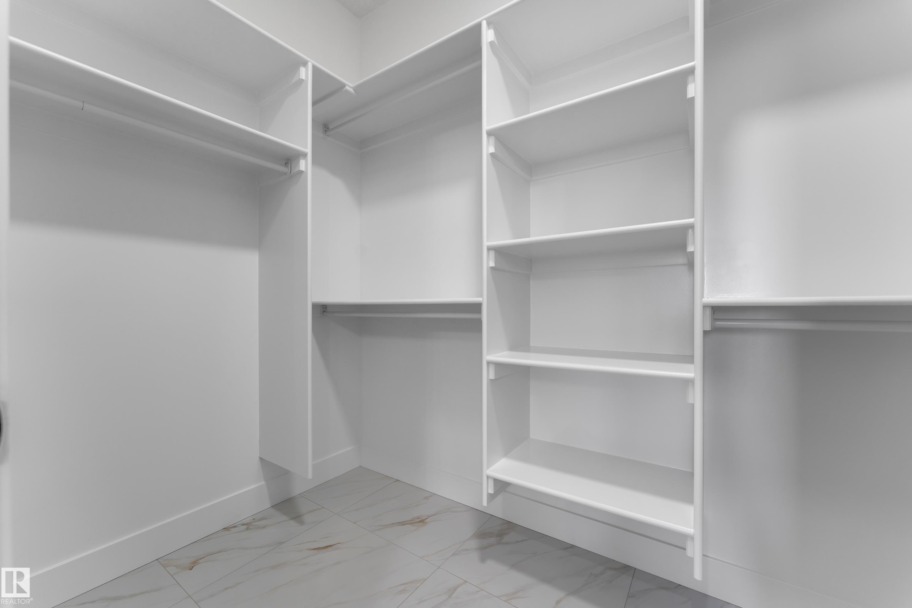 Built-in closet system with multiple shelving units and hanging rods, complemented by white walls and tile flooring - 4212 63 Street, Beaumont, AB