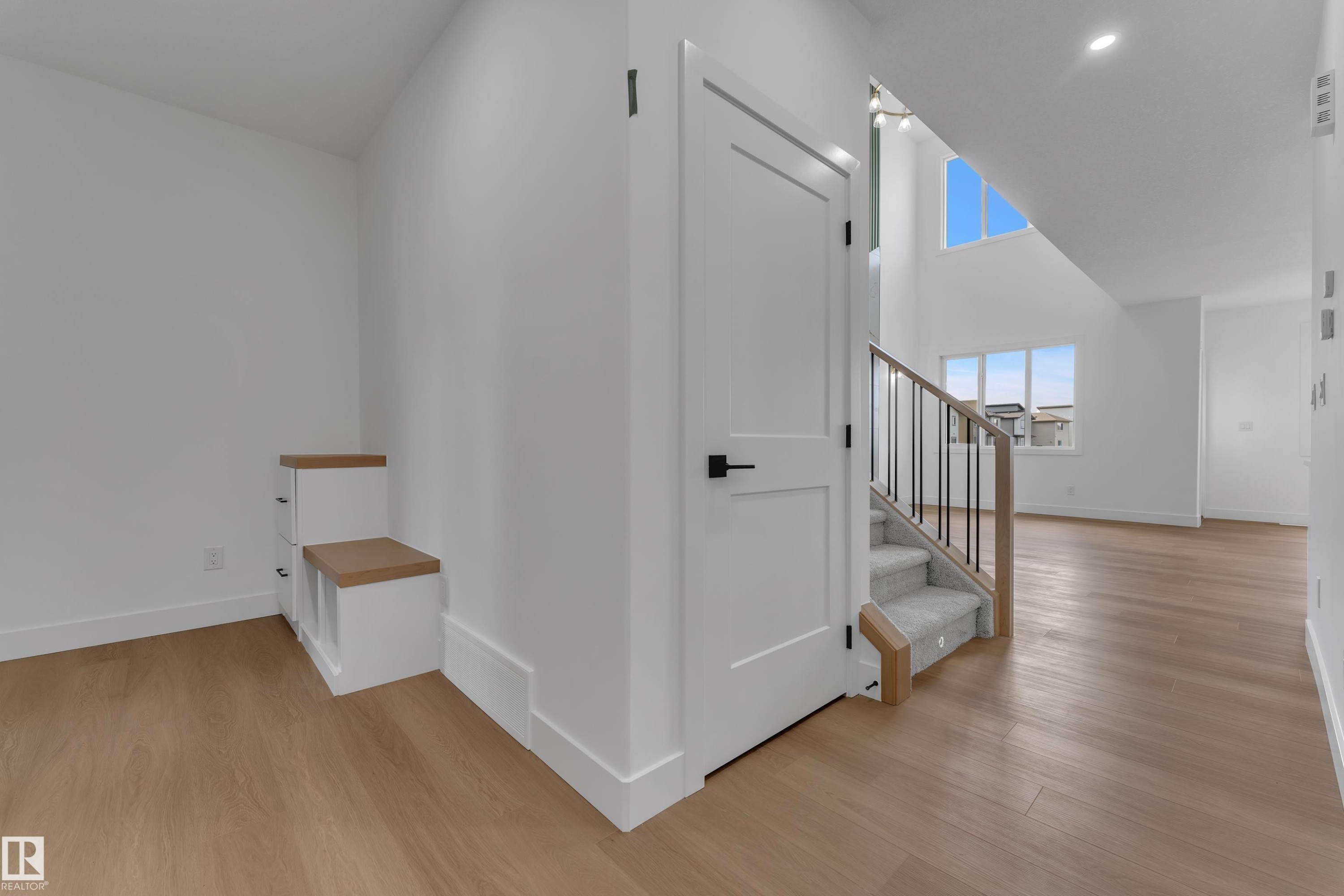 Hardwood-finish flooring throughout, white walls, built-in storage bench with wood-finish tops, white interior doors with black hardware, and an open staircase with carpeted treads and metal balusters - 4212 63 Street, Beaumont, AB