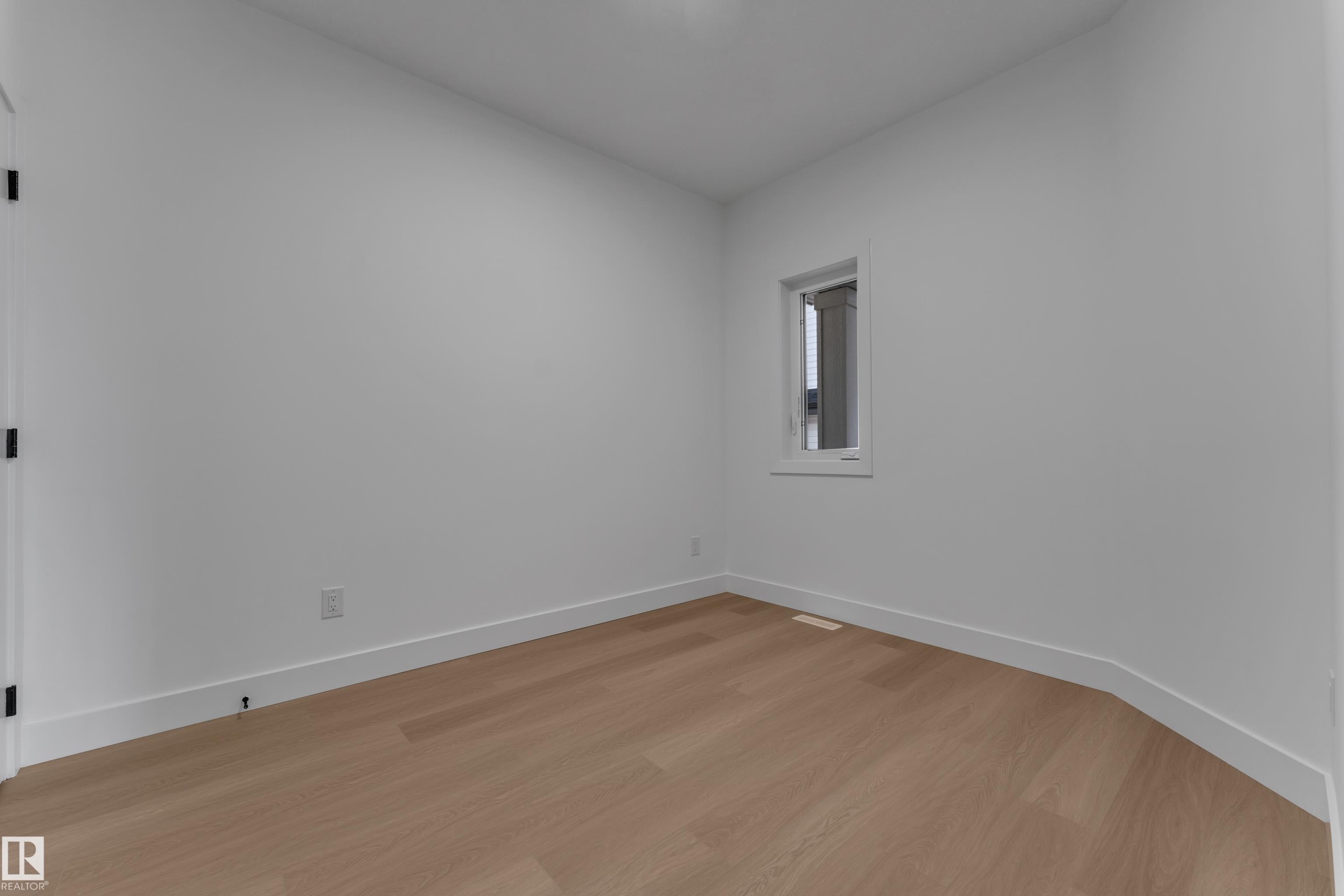 Light wood-finish flooring with white baseboards, a white door with matte black hardware, and a single window with white trim - 4212 63 Street, Beaumont, AB