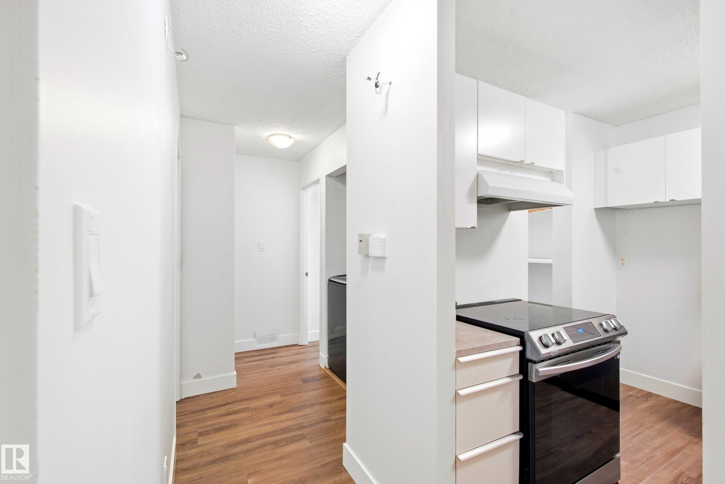Wood-finish flooring throughout, bright white walls, contemporary white cabinetry, stainless steel range with overhead hood fan, and integrated shelving - 258 Surrey Gardens Nw, Edmonton, AB
