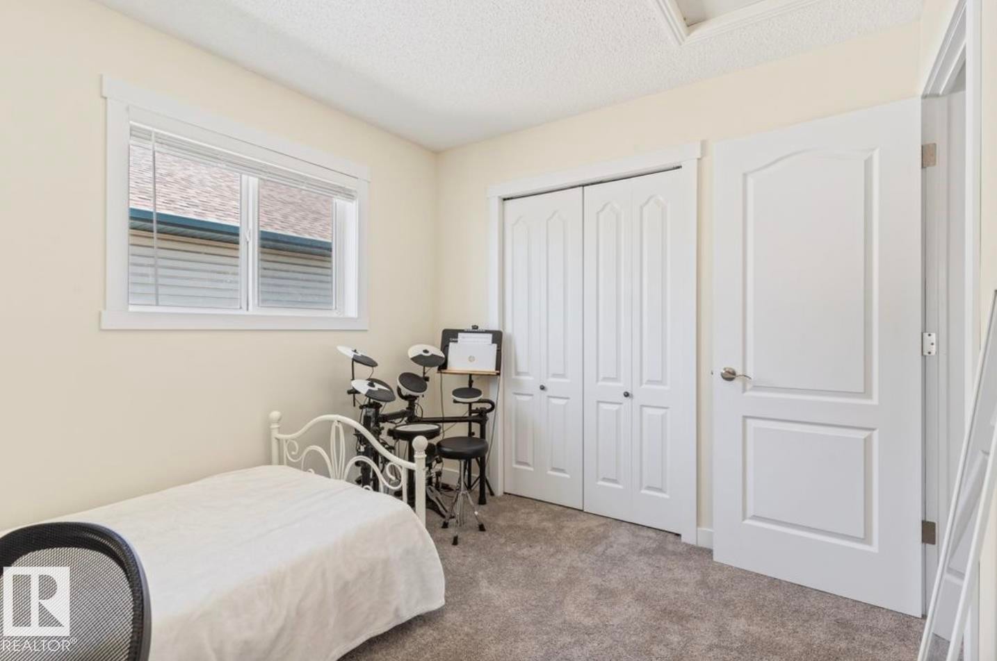 Carpeted room featuring a window with blinds, white trim, a closet with bi-fold doors, and a paneled interior door - 1007 Macewan Close Sw, Edmonton, AB - Indoor Photo Showing Bedroom
