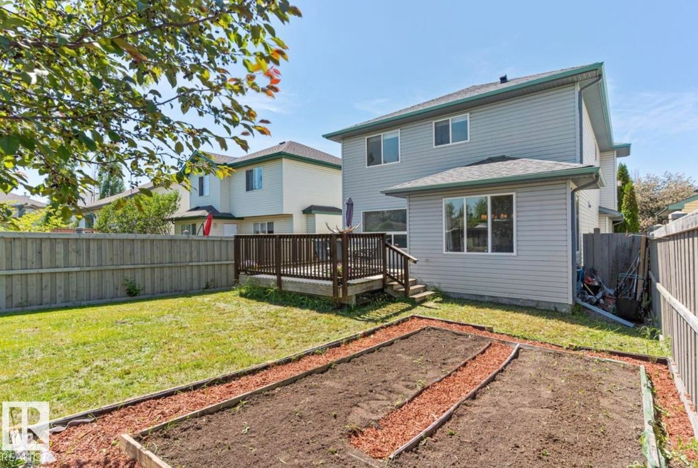 Rear property exterior featuring a wood deck, manicured lawn, and raised garden beds - 1007 Macewan Close Sw, Edmonton, AB - Outdoor