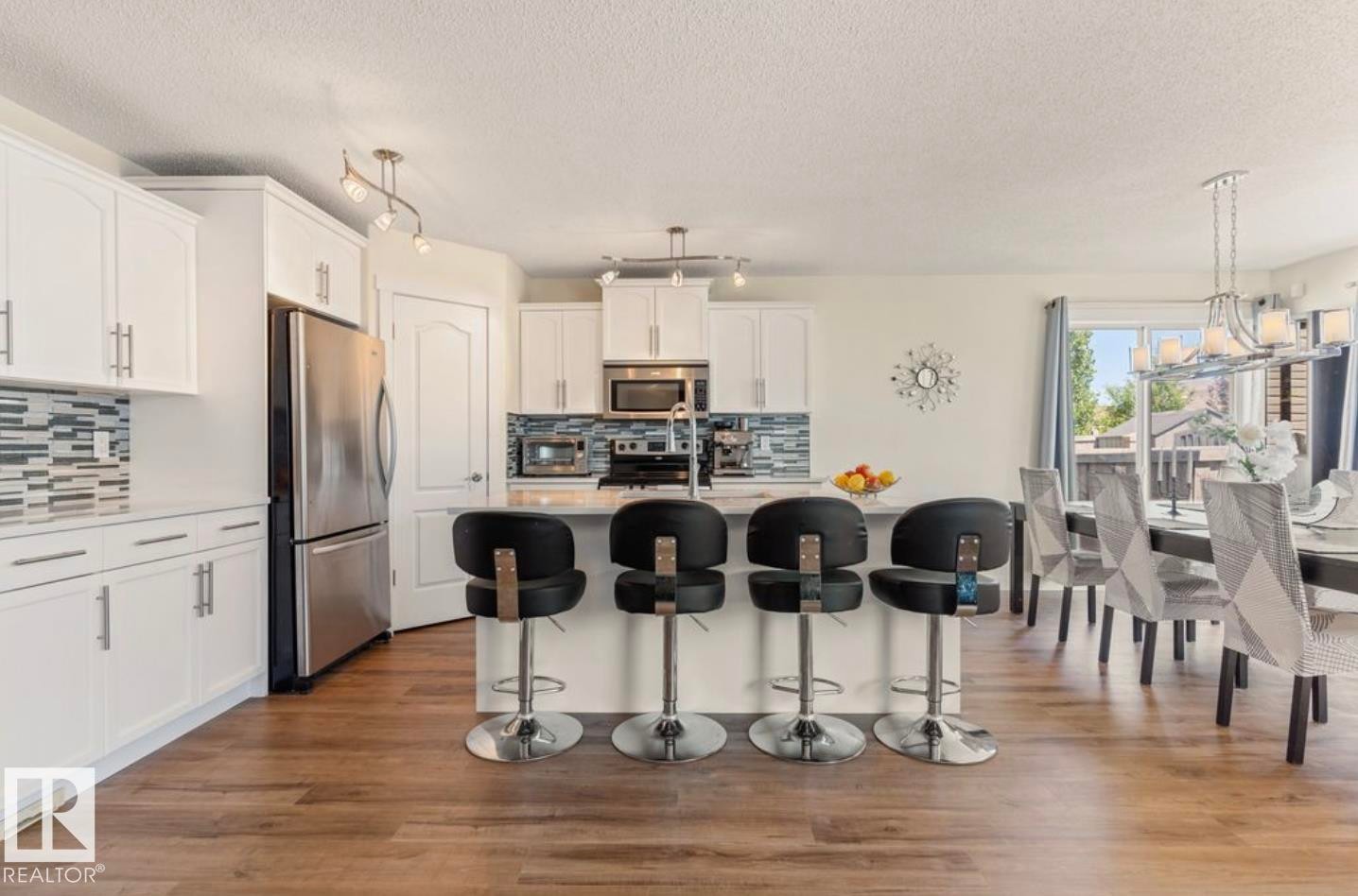 Kitchen featuring an island with seating, white cabinetry, stainless steel appliances, and wood-finish flooring - 1007 Macewan Close Sw, Edmonton, AB - Indoor Photo Showing Kitchen With Stainless Steel Kitchen With Upgraded Kitchen