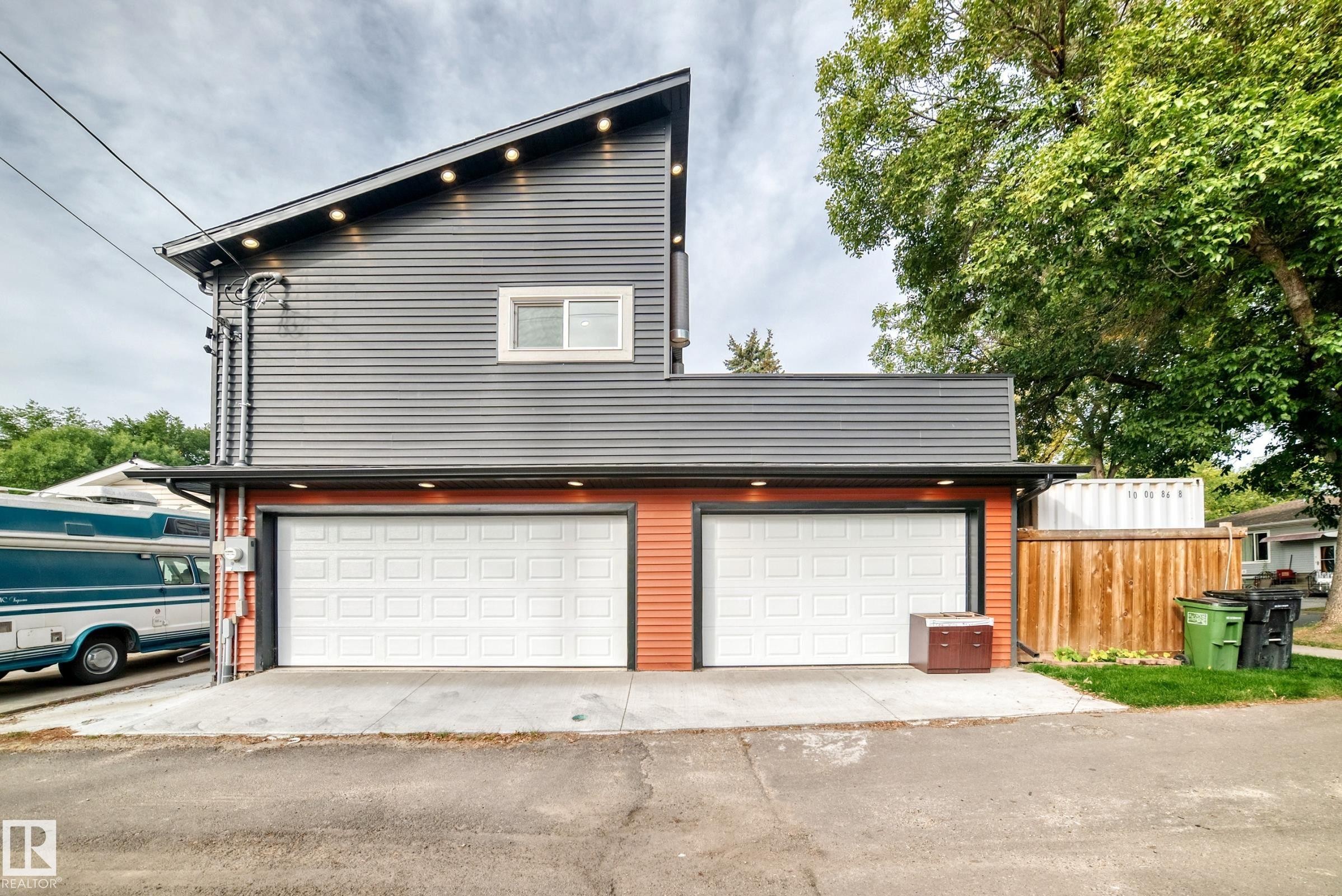 Modern two-story residence featuring a newly constructed garage with dual white panel doors, horizontal metal accents, and warm wood-finish fencing - 12045 64 Street Nw, Edmonton, AB