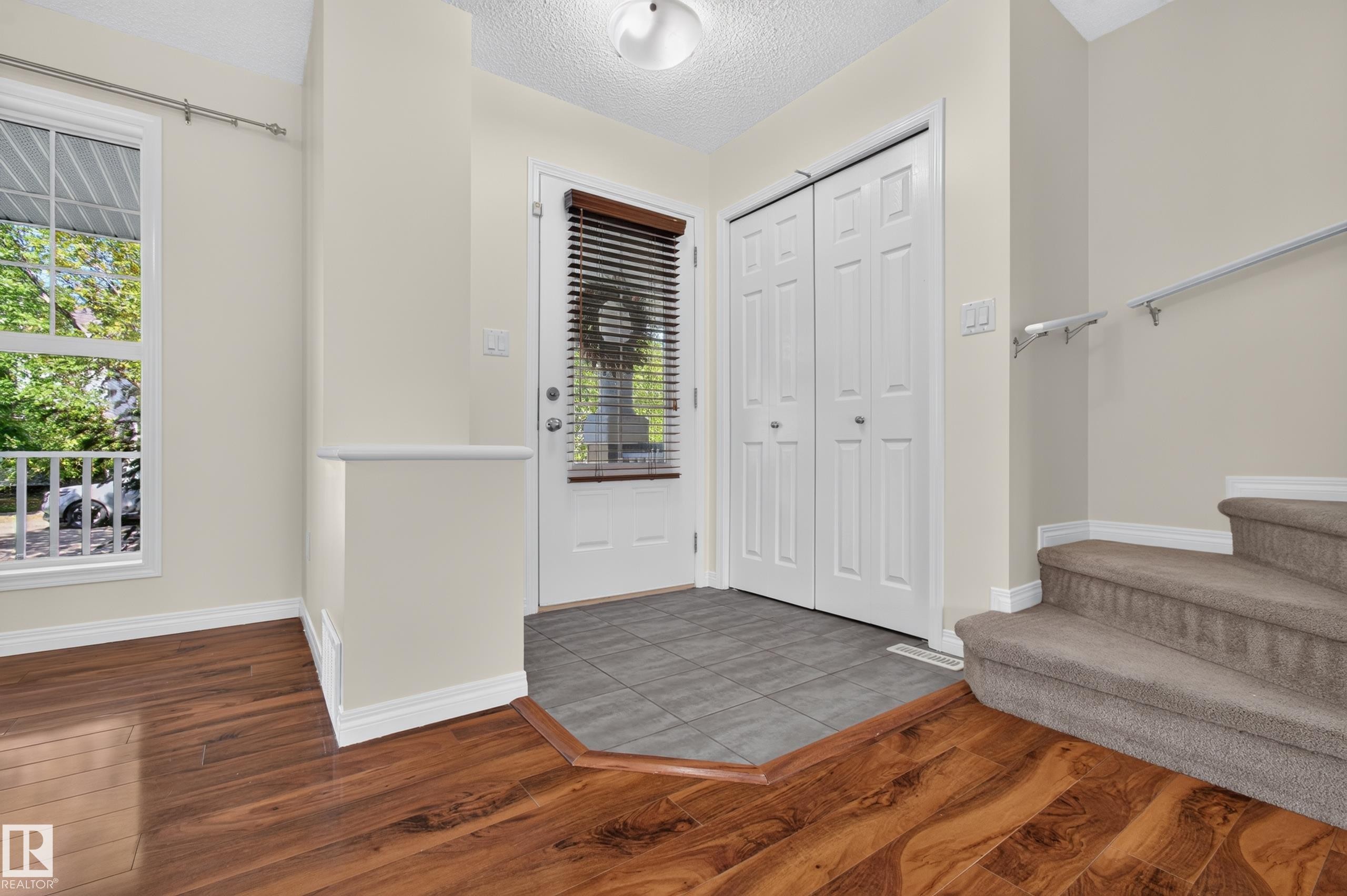 Entryway featuring wood-finish flooring, tiled landing, bi-fold closet doors, and staircase with carpeting - 6933 21A Avenue Sw, Edmonton, AB