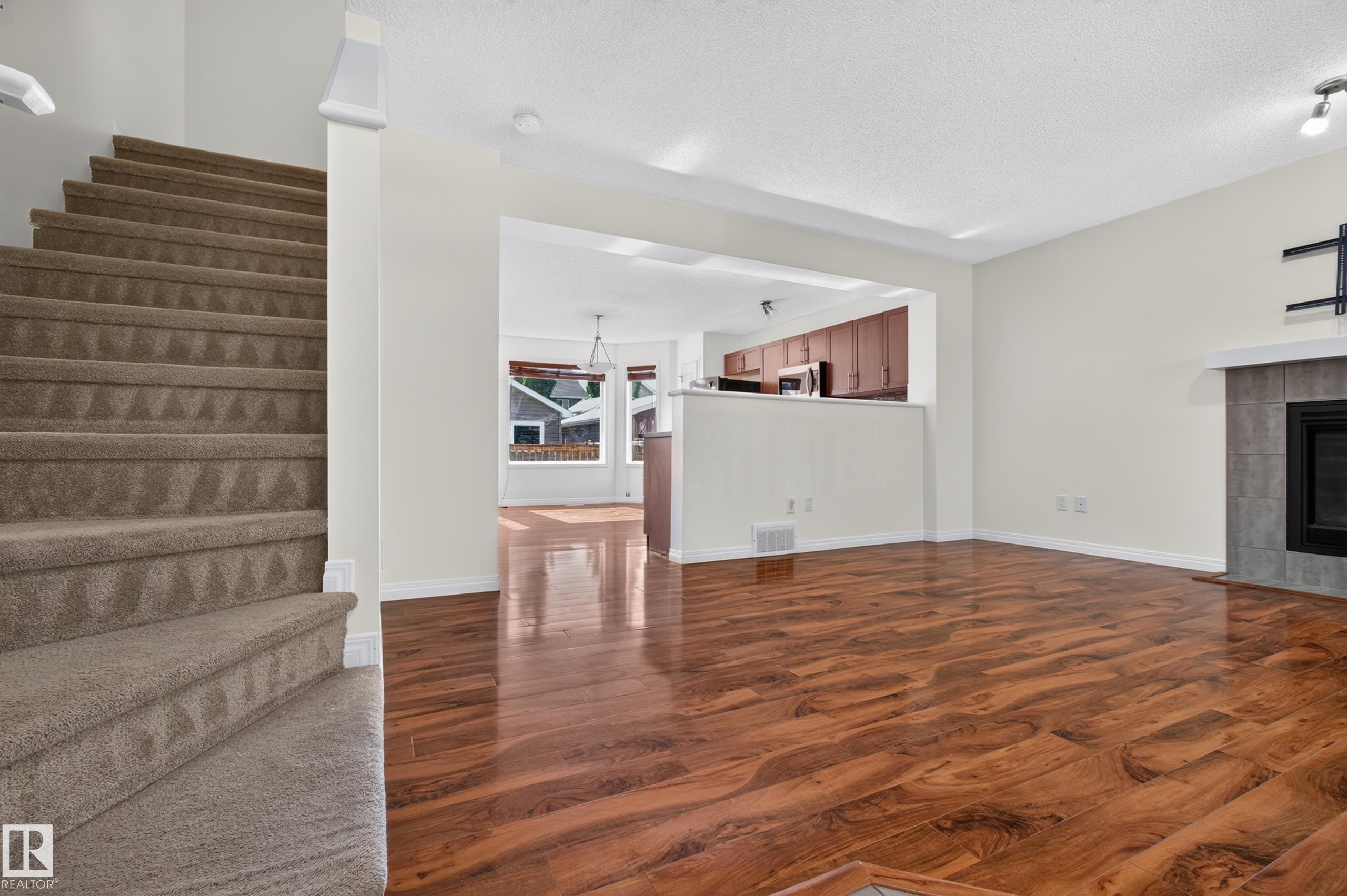 Expansive main living area featuring wood-finish flooring, a tiled fireplace with a mantel, and an open concept layout - 6933 21A Avenue Sw, Edmonton, AB