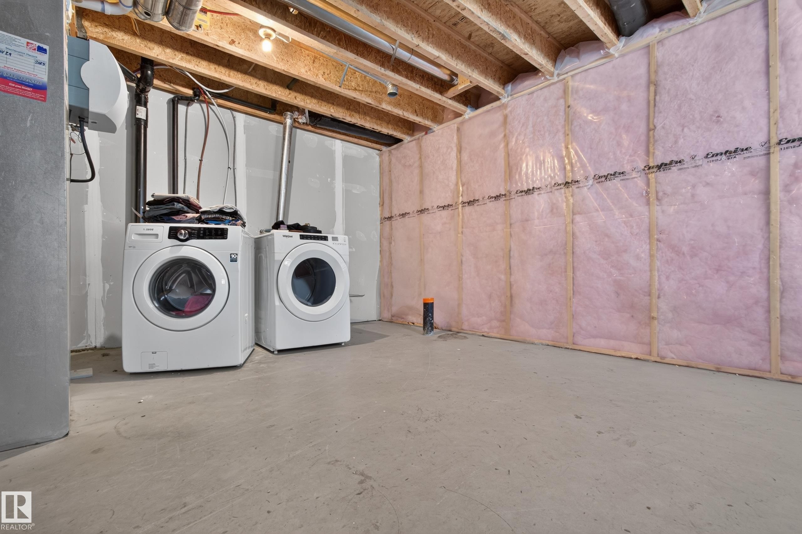 Concrete flooring, exposed ceiling joists, insulated wall framing, and white front-load washer and dryer units - 6933 21A Avenue Sw, Edmonton, AB