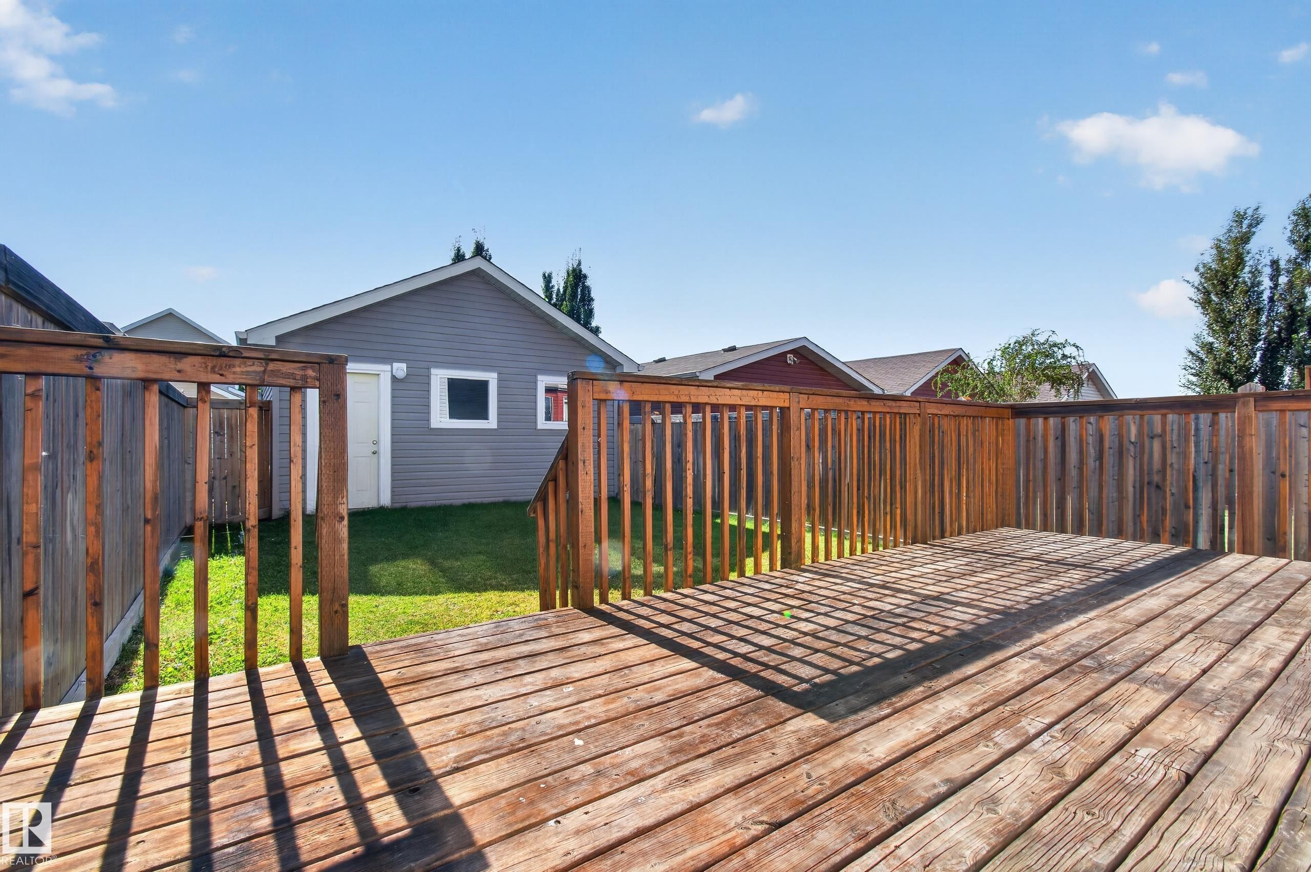 Expansive wooden deck with railing, leading to a manicured lawn - 6933 21A Avenue Sw, Edmonton, AB