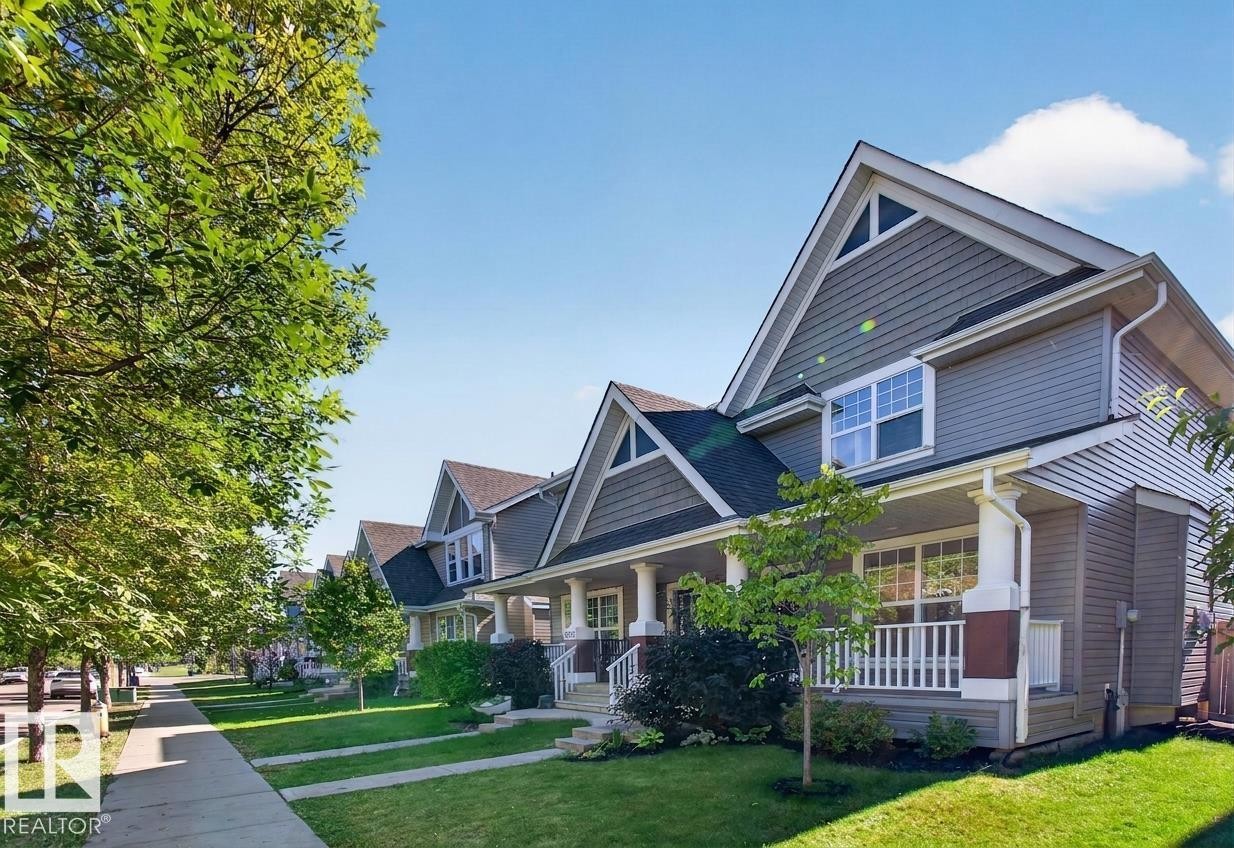 Exterior with shingle siding, covered front porch, gabled roofline, mature trees, and a manicured lawn - 6933 21A Avenue Sw, Edmonton, AB