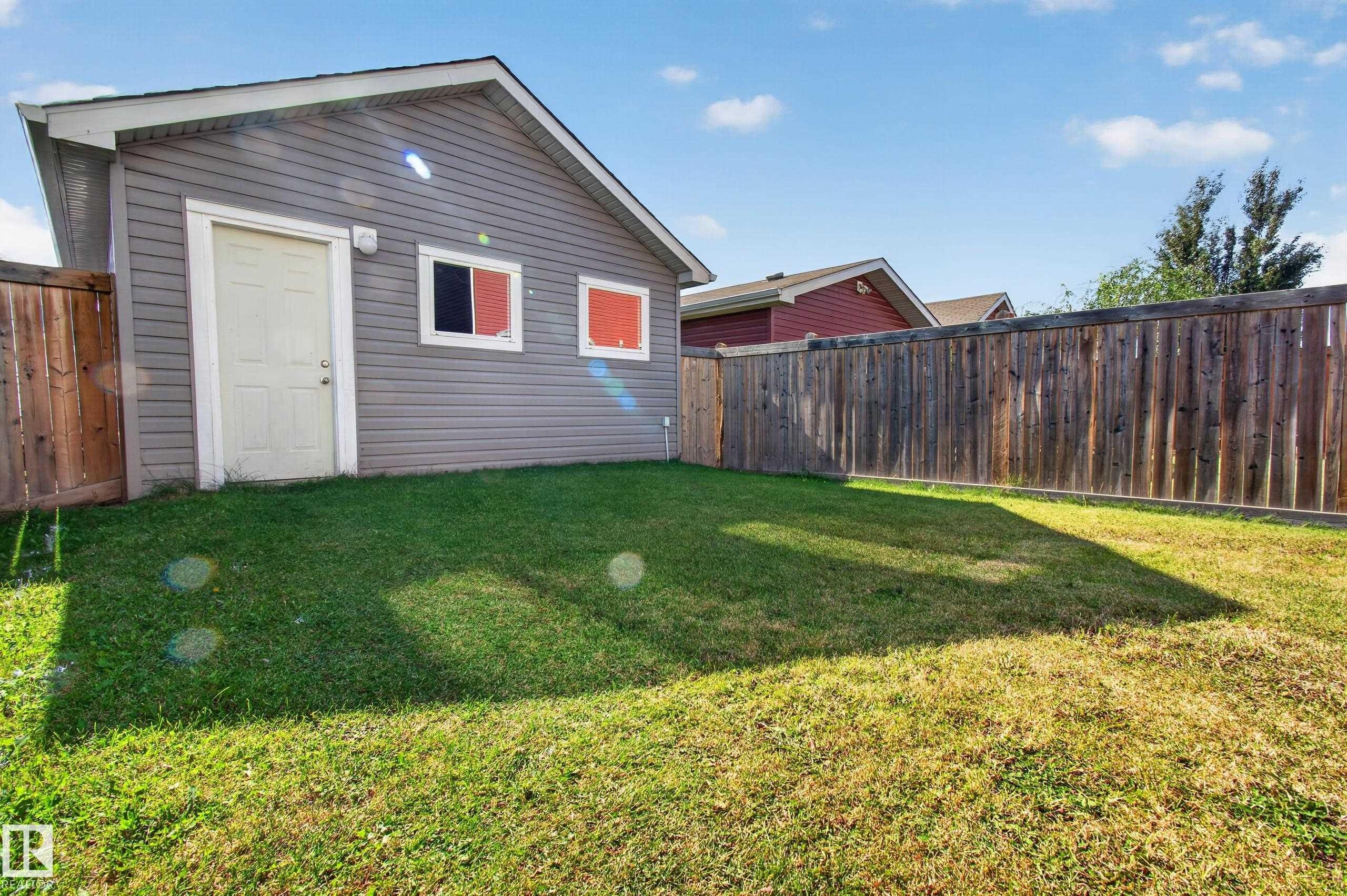 Rear detached structure with gray siding, a white service door, and two windows - 6933 21A Avenue Sw, Edmonton, AB