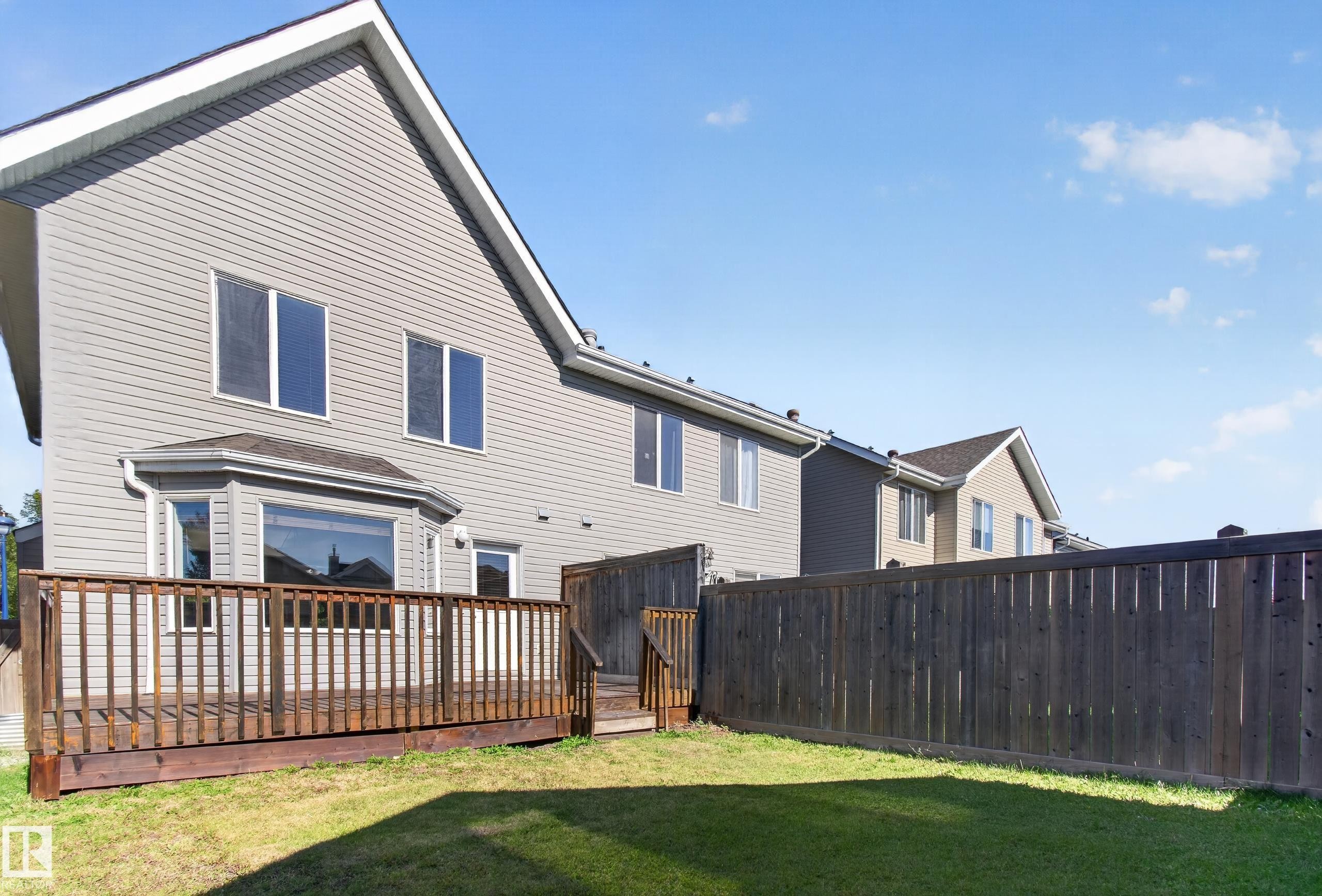 Expansive backyard featuring a wood deck, manicured lawn, and privacy fencing - 6933 21A Avenue Sw, Edmonton, AB