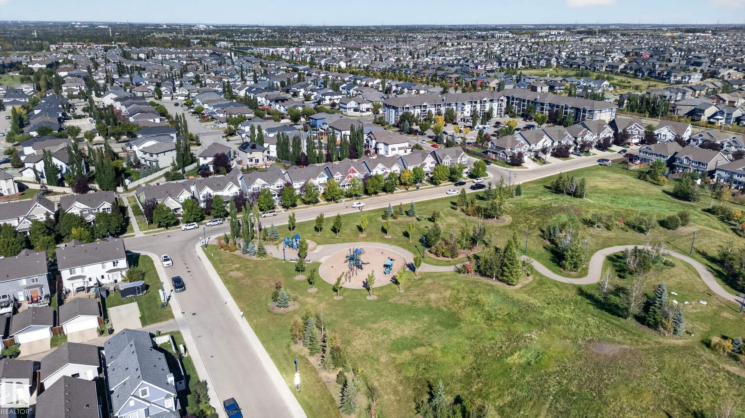 Expansive neighborhood featuring residential properties, a dedicated park area with playground equipment, walking paths, and mature trees - 6933 21A Avenue Sw, Edmonton, AB