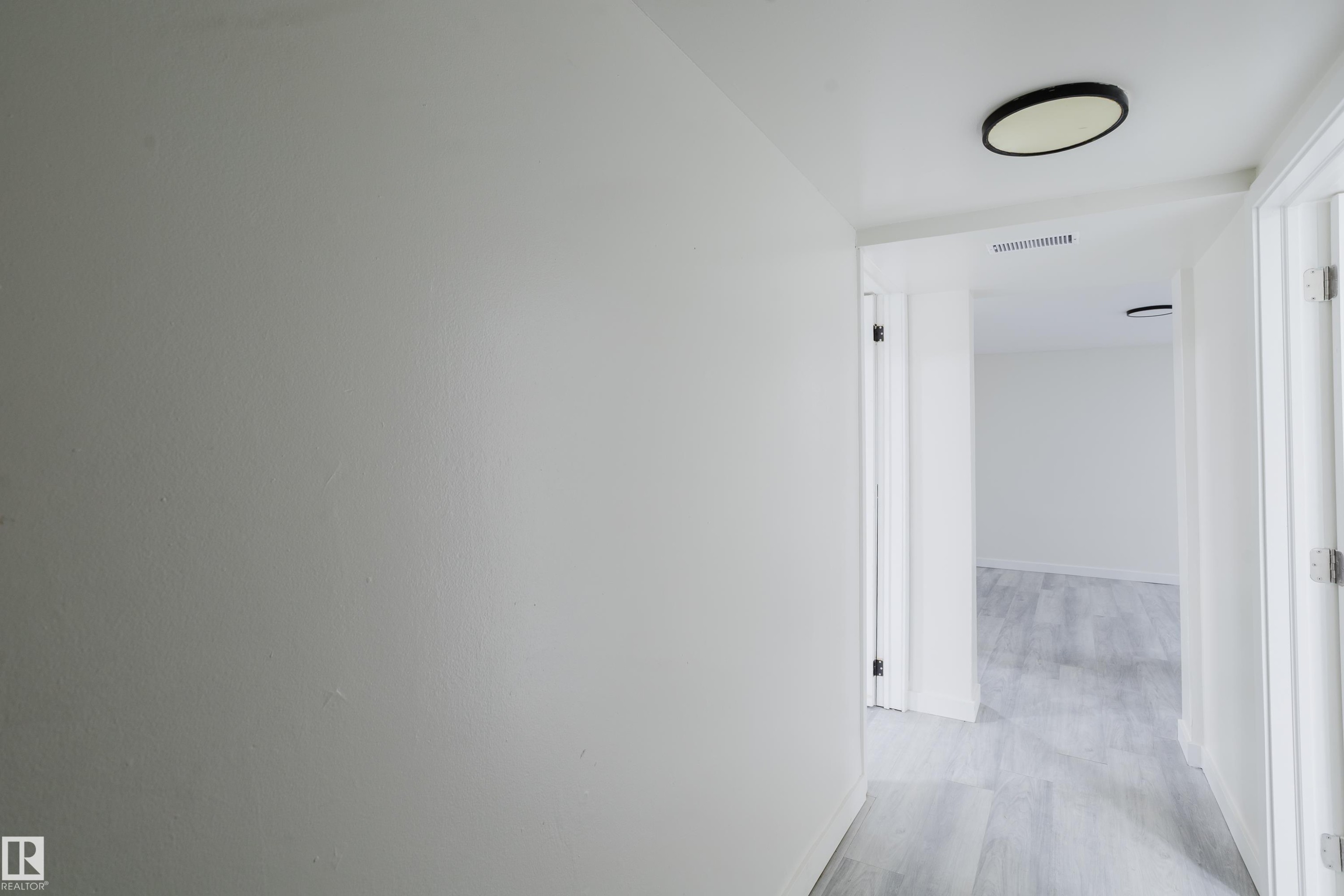 Hallway featuring flush-mount ceiling lighting, crisp white paint, and wood-finish flooring - 11134 11138 116 Street Nw, Edmonton, AB