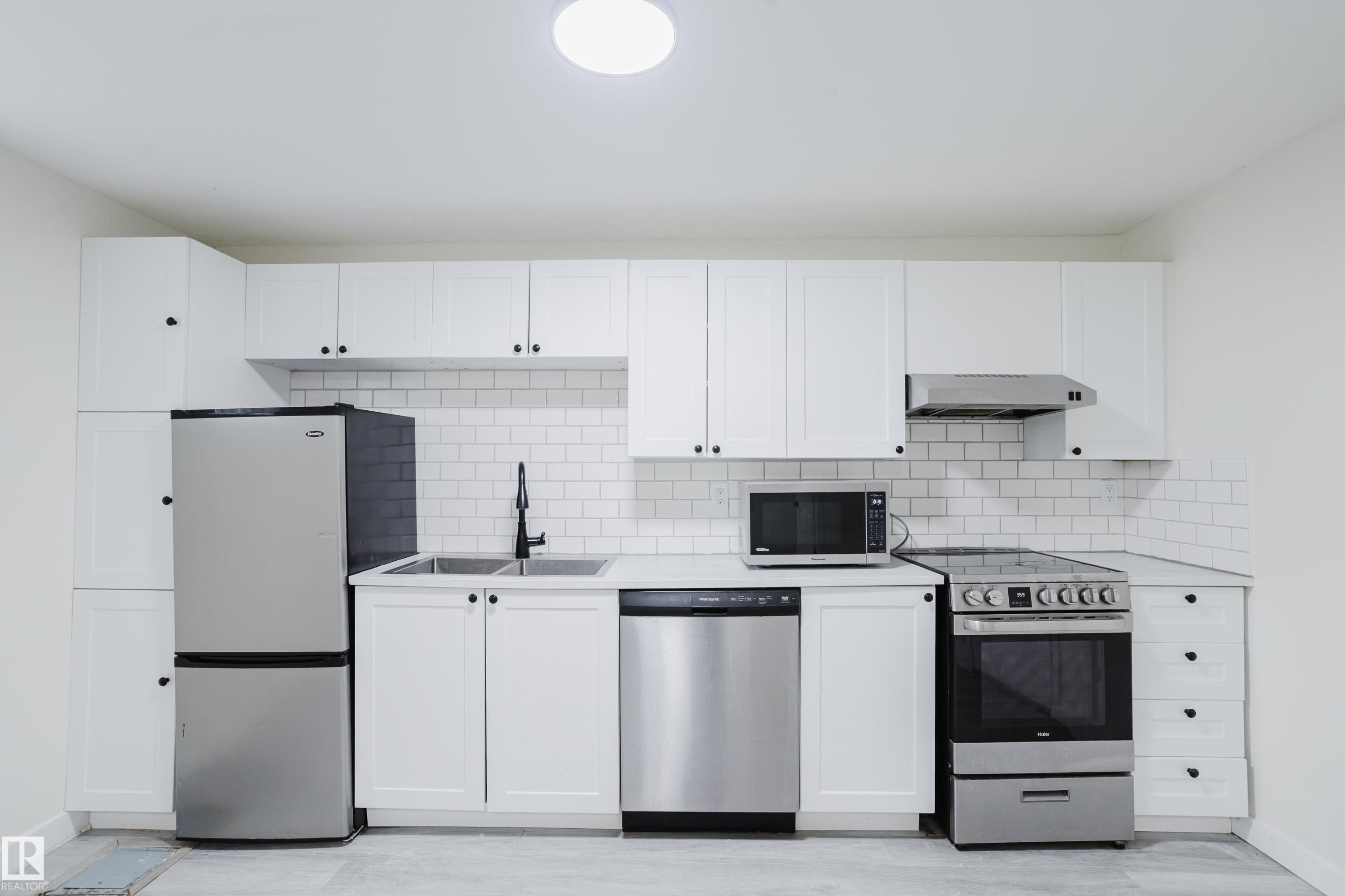 White shaker cabinetry with dark hardware, stainless steel appliances, dual basin sink with matte black faucet, white subway tile backsplash, and light-toned flooring - 11134 11138 116 Street Nw, Edmonton, AB