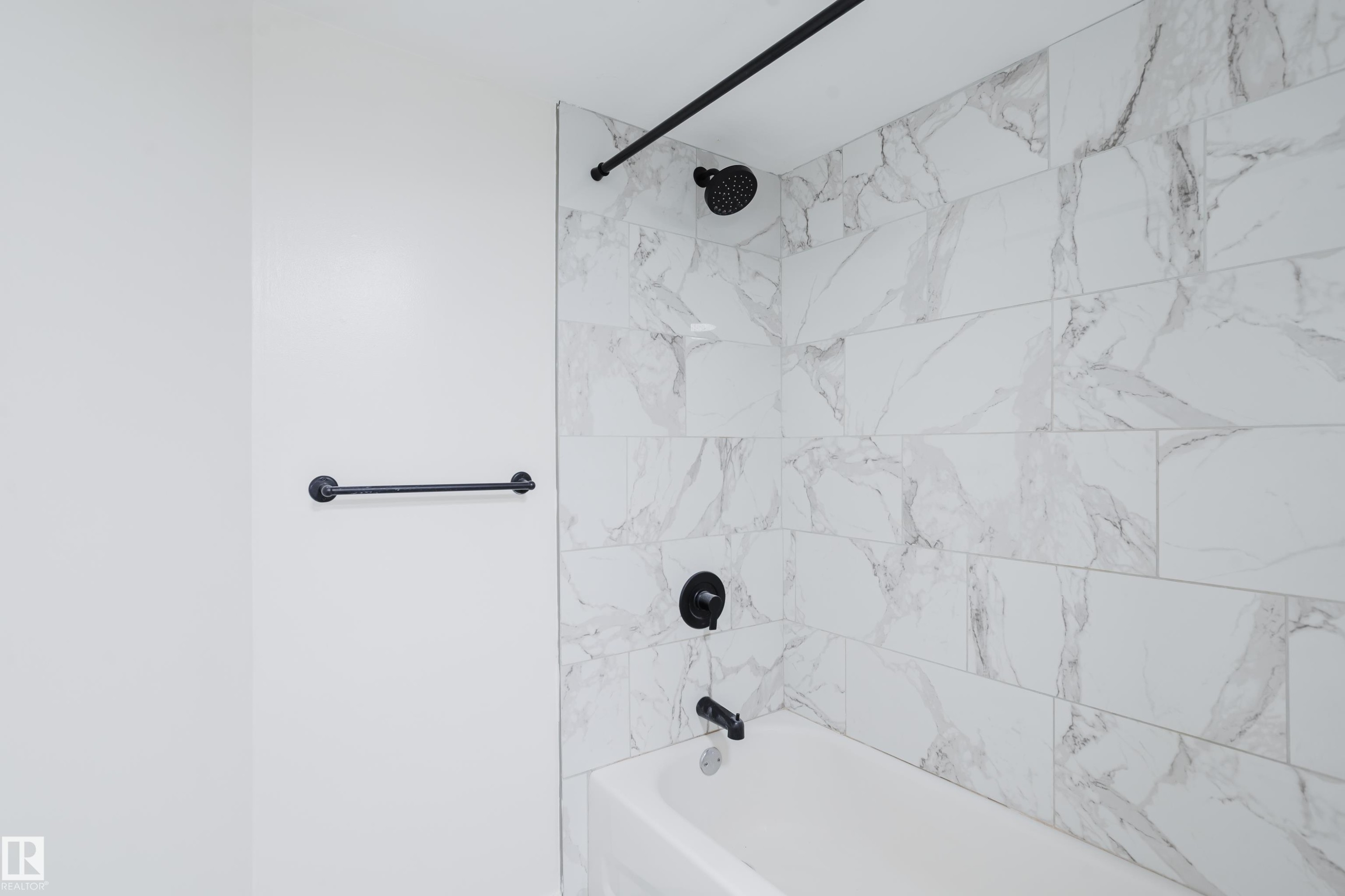 Tub and shower combination featuring large format tile surround, matte black fixtures, and a coordinating towel bar - 11134 11138 116 Street Nw, Edmonton, AB