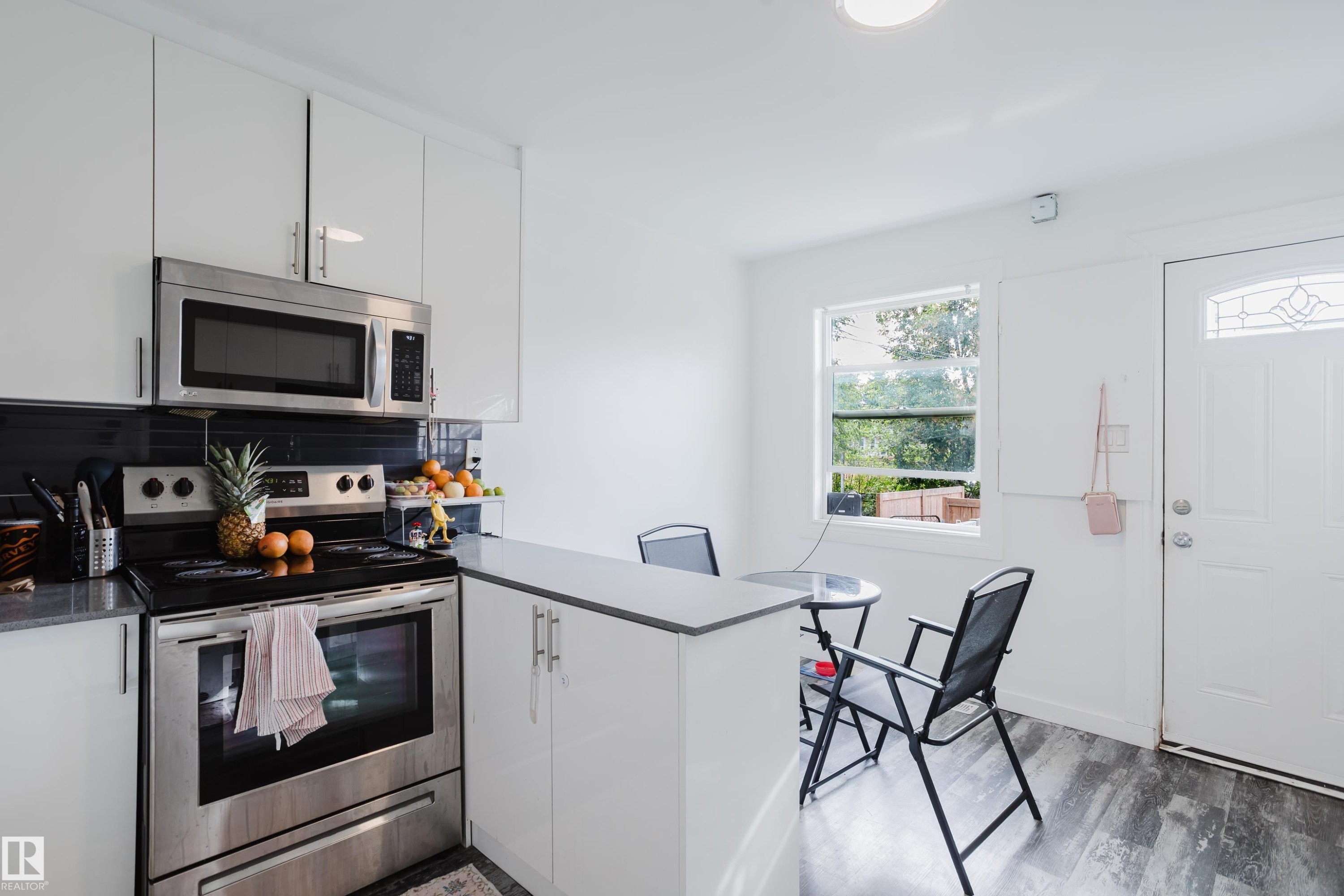 Kitchen featuring stainless steel appliances, white cabinetry, dark countertop, and wood-finish flooring - 11134 11138 116 Street Nw, Edmonton, AB
