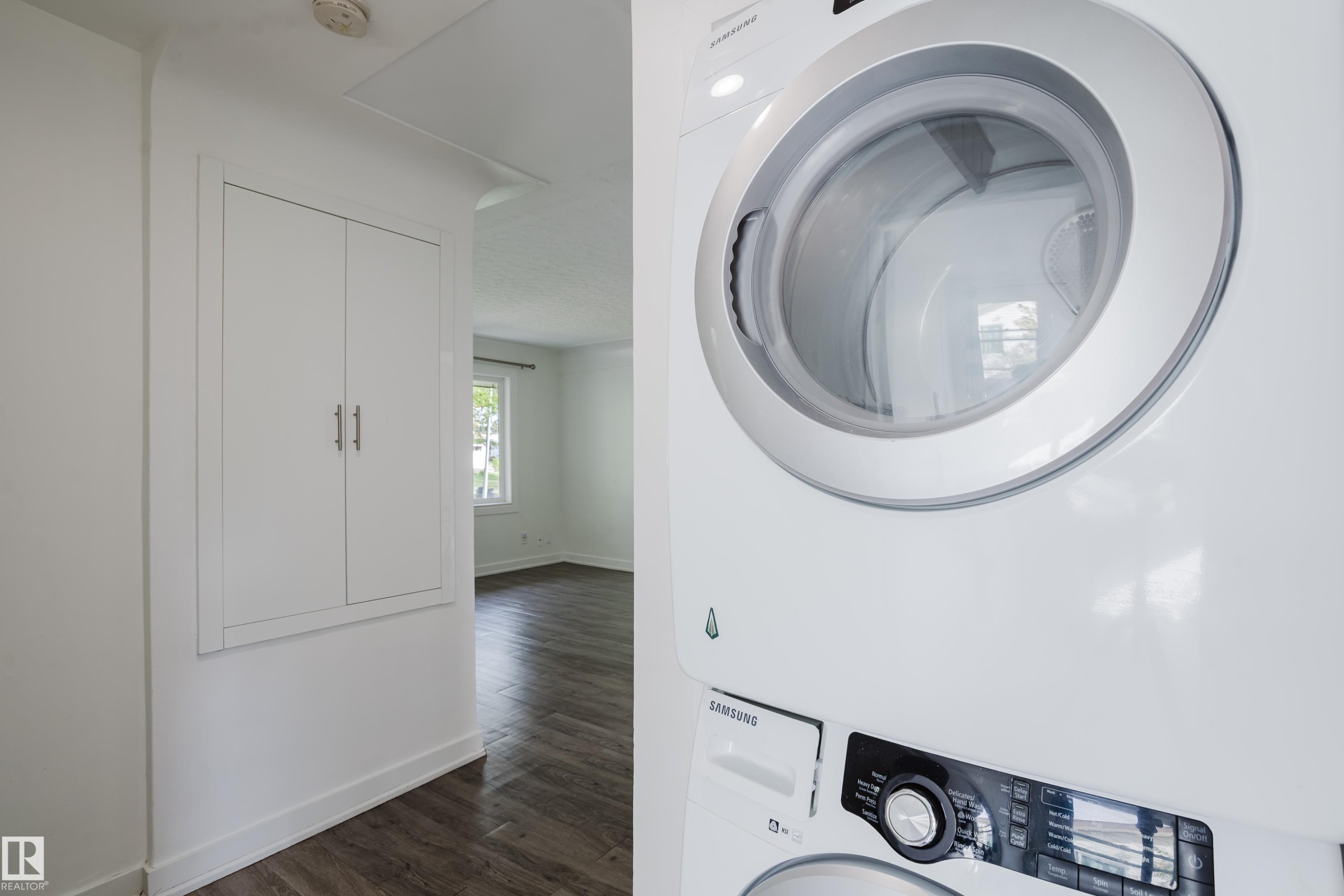 White stacked washer and dryer unit, built-in storage cabinetry, and wood-finish flooring - 11134 11138 116 Street Nw, Edmonton, AB
