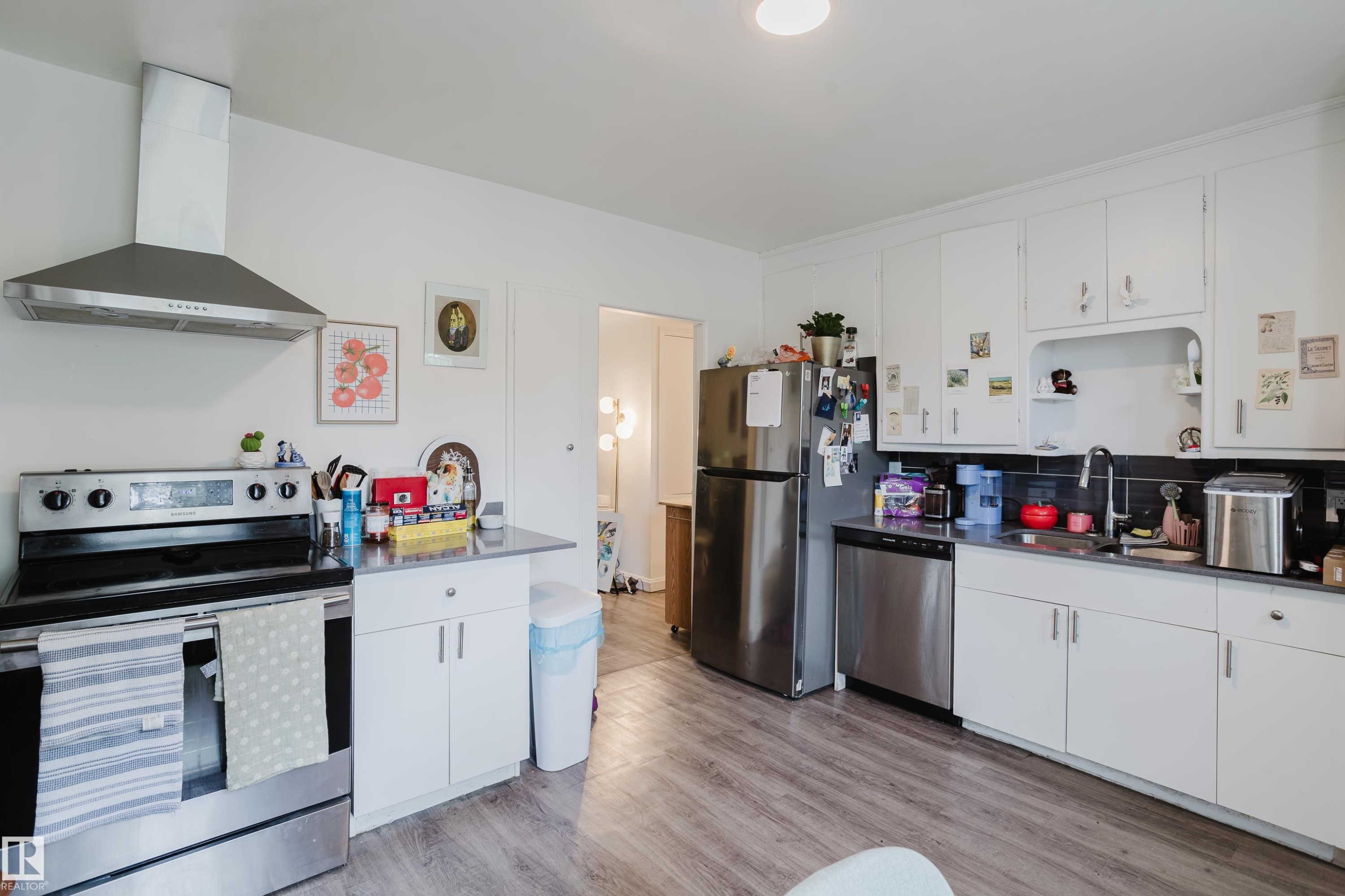 Kitchen featuring white cabinetry, wood-finish flooring, stainless steel appliances, and a black tile backsplash - 11134 11138 116 Street Nw, Edmonton, AB