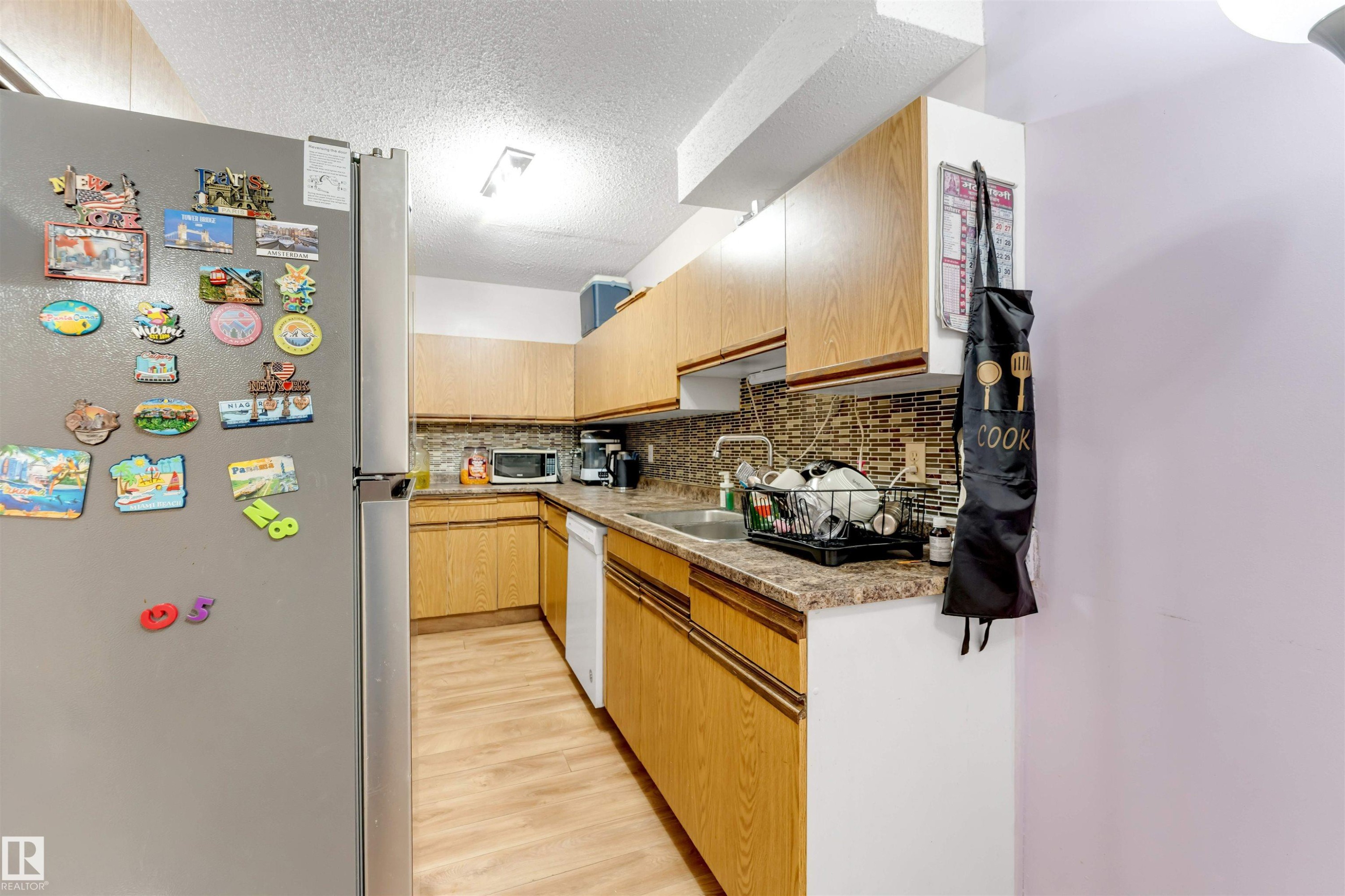 Wood-finish flooring, wood-finish cabinetry, patterned tile backsplash, double basin sink, and recessed lighting - #101 49 Akins Dr, St. Albert, AB