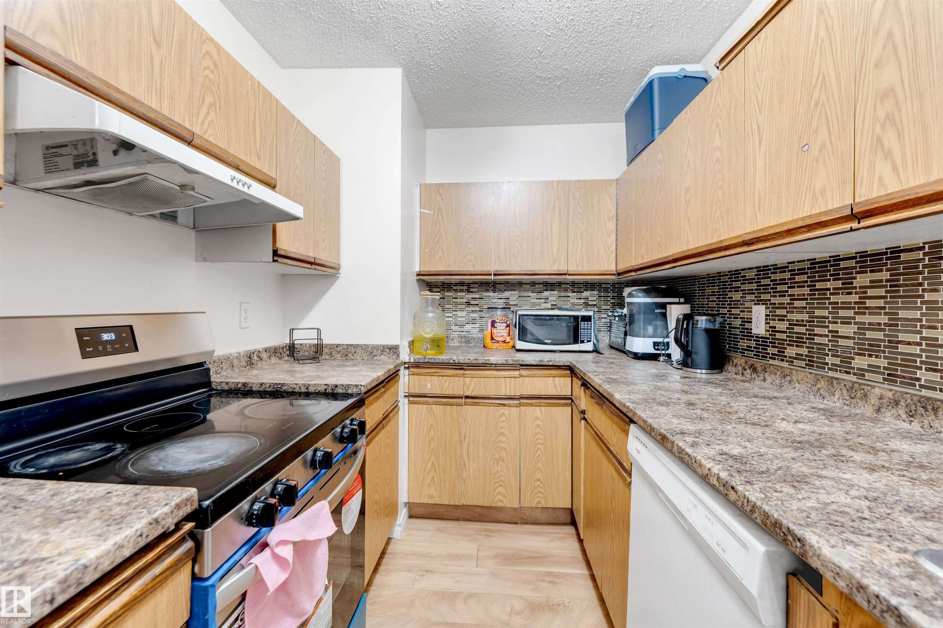 Kitchen featuring wood-finish cabinetry, patterned laminate countertops, a tile backsplash, stainless steel range, and a dishwasher - #101 49 Akins Dr, St. Albert, AB