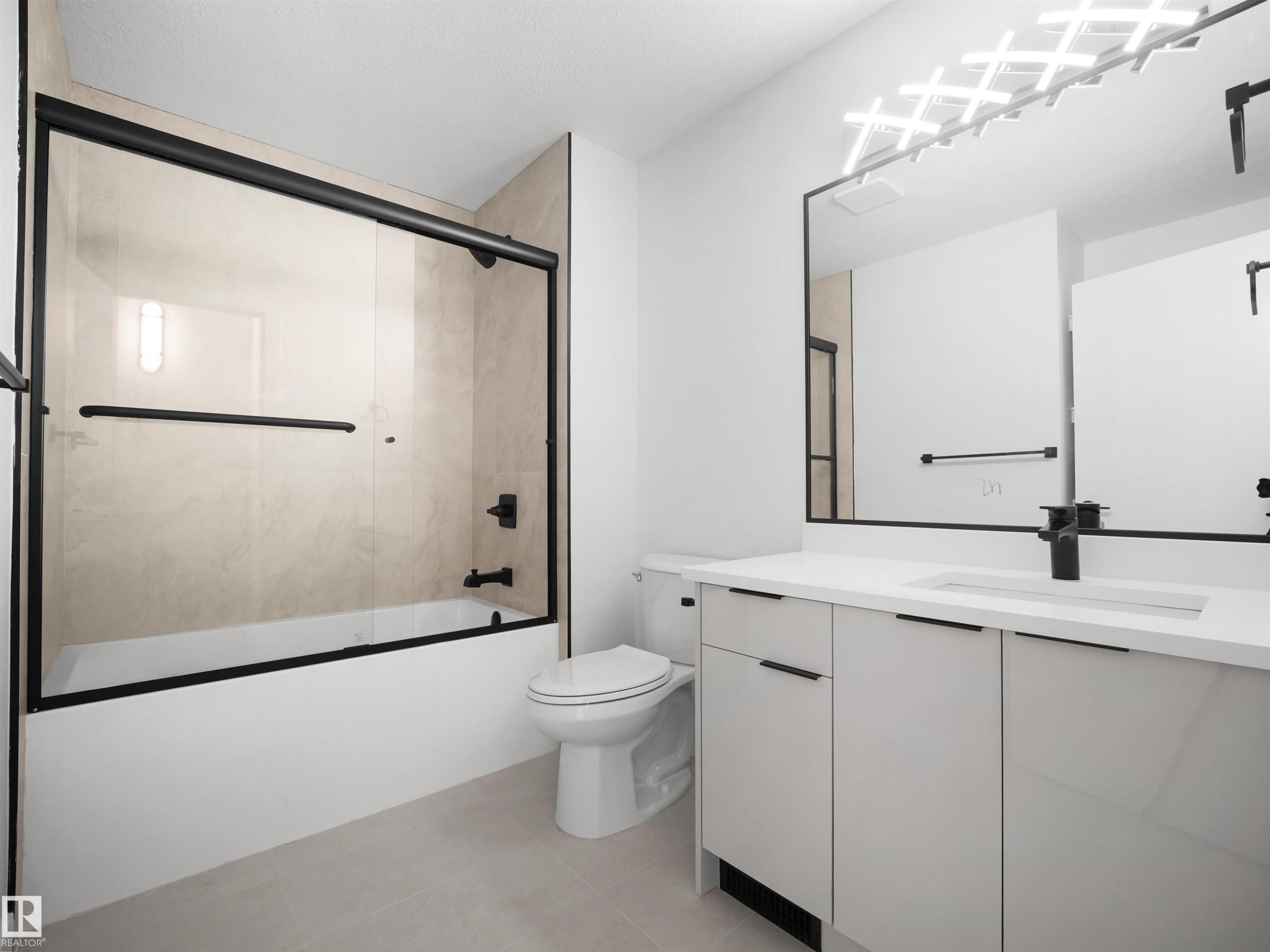 Bathroom featuring a vanity with an integrated sink, black framed mirror, and a tub with a sliding glass door - 12C Twin Terrace Nw, Edmonton, AB