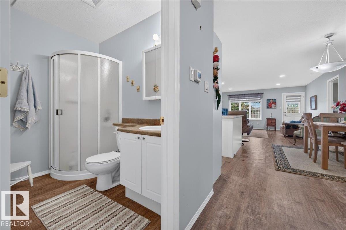 Bathroom with a corner shower enclosure, white vanity cabinet, and wood-finish flooring - #125 4610 50 Ave, Stony Plain, AB