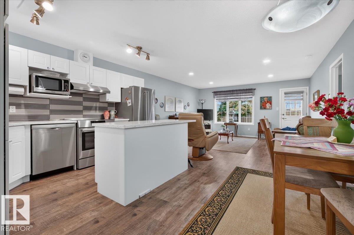 Open concept living space featuring wood-finish flooring, white cabinetry, stainless steel appliances, a white kitchen island, and recessed lighting - #125 4610 50 Ave, Stony Plain, AB