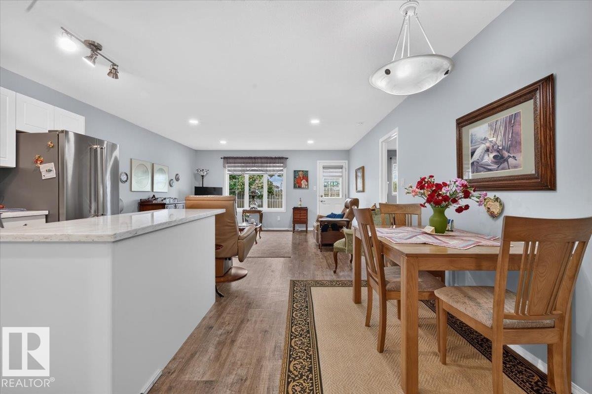 Open-concept living space with wood-finish flooring, recessed lighting, and a kitchen island featuring a light-colored countertop - #125 4610 50 Ave, Stony Plain, AB
