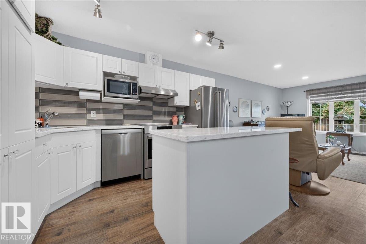 Kitchen featuring white cabinetry, stainless steel appliances, a multi-tone tile backsplash, and light-colored countertops - #125 4610 50 Ave, Stony Plain, AB