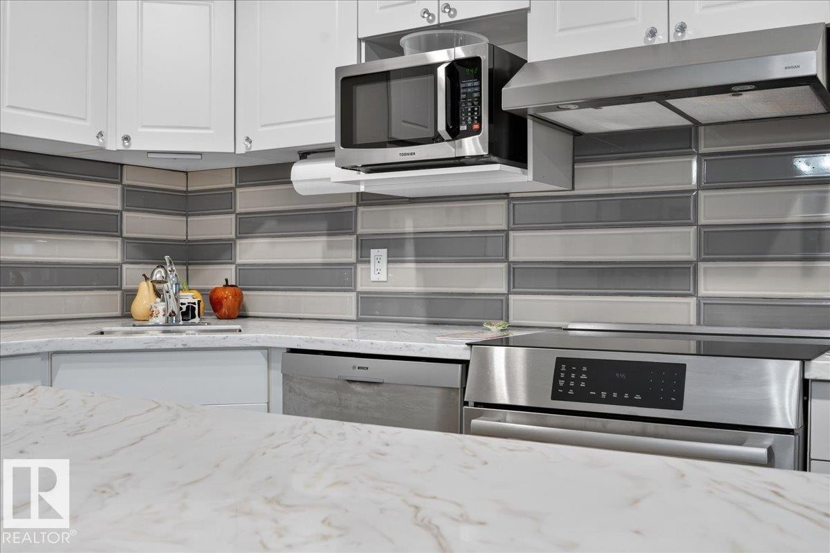 White cabinetry, stainless steel appliances, patterned tile backsplash, under-cabinet microwave, and a stainless steel range hood - #125 4610 50 Ave, Stony Plain, AB